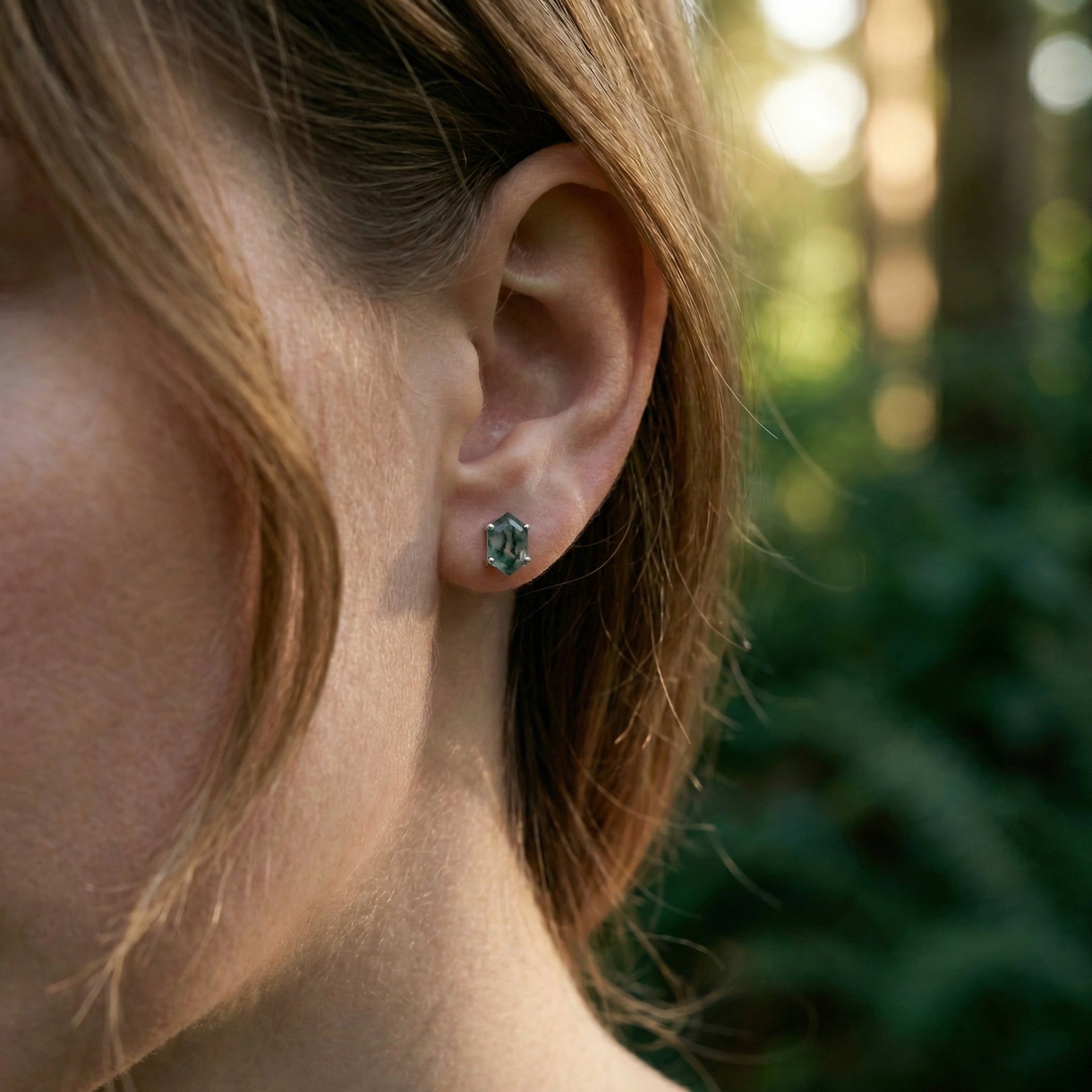Side view of a model wearing a coffin cut moss agate sterling silver stud earring in an outdoor setting.