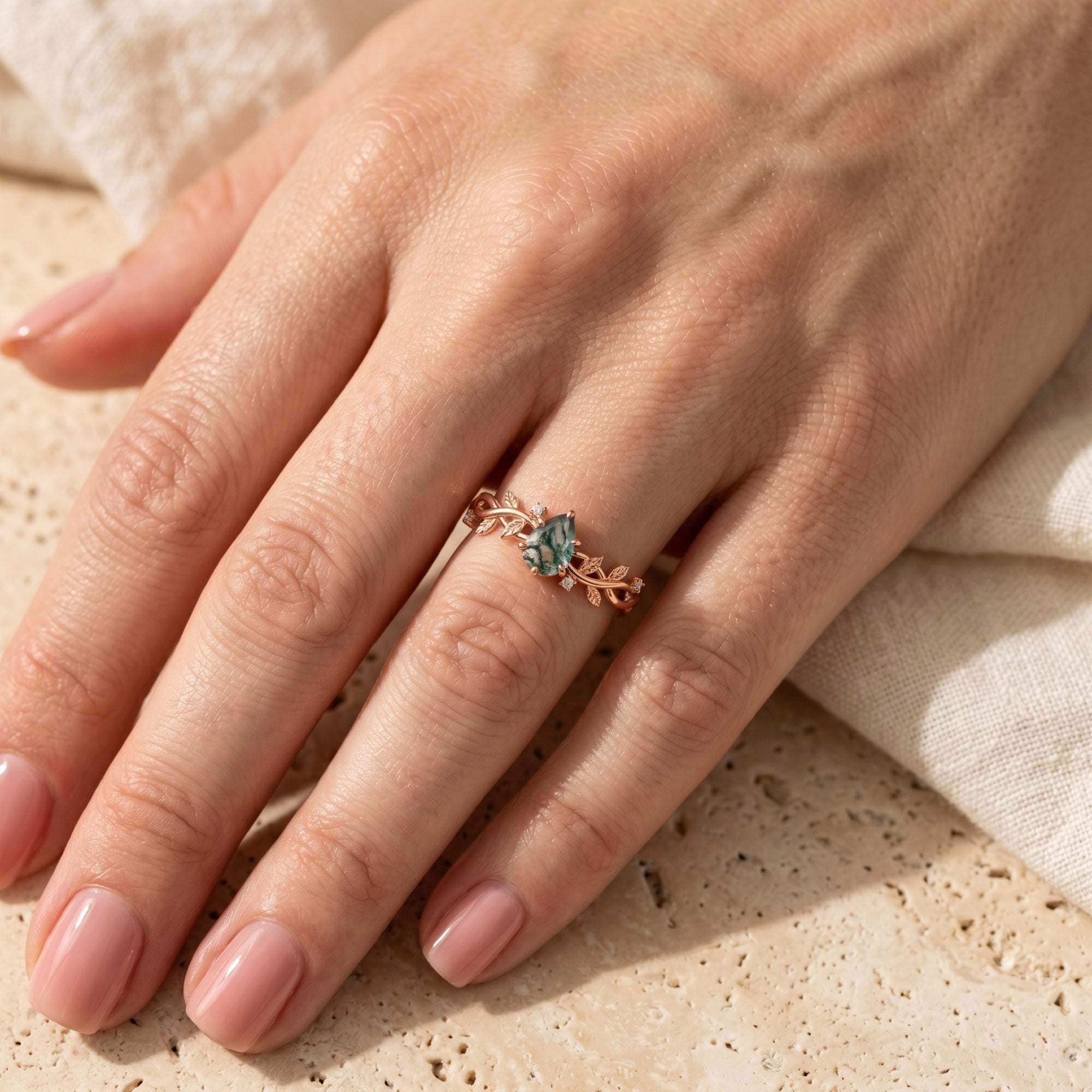 Rose gold moss agate ring with vine band worn on a hand.