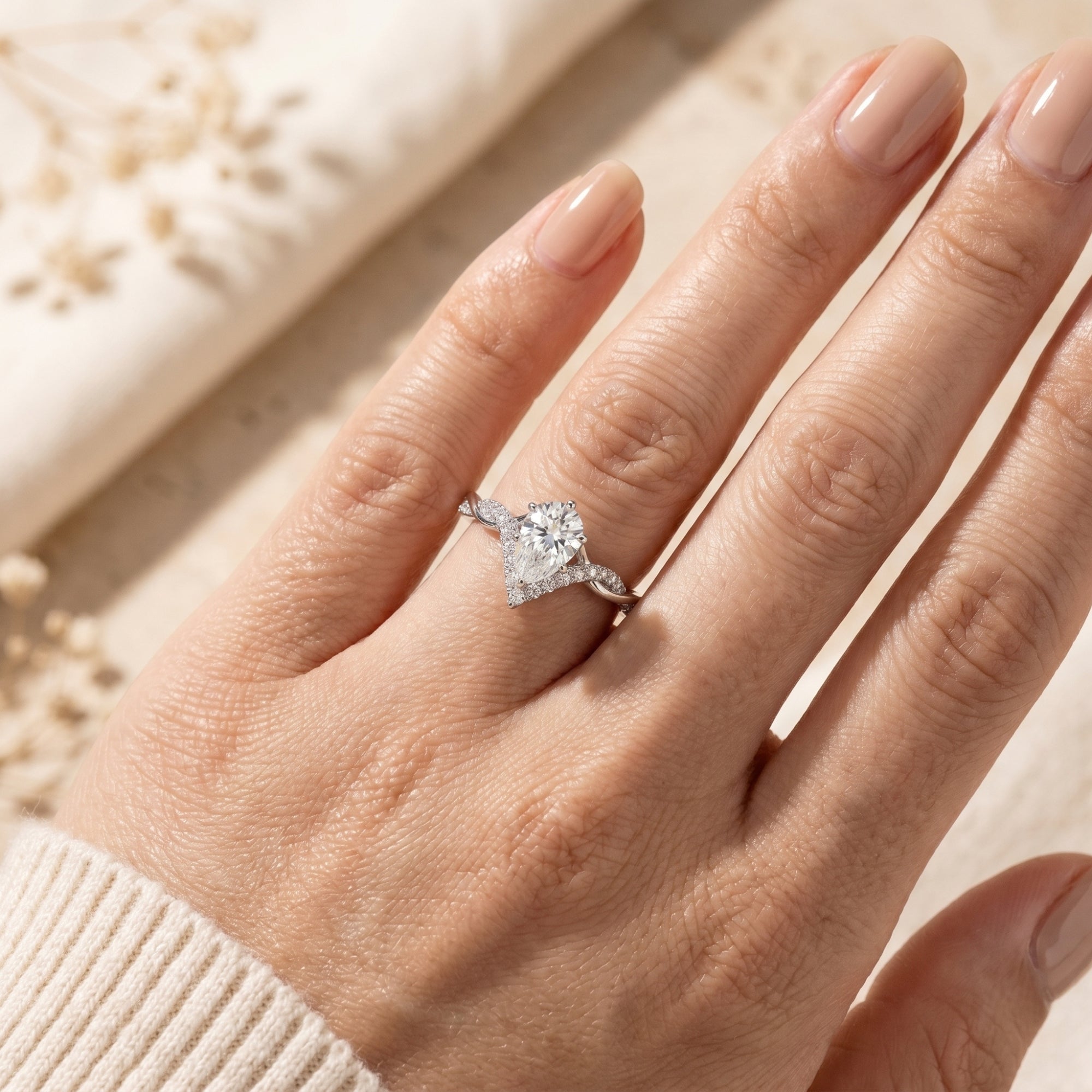 Top-down view of the silver Araminta pear-cut moissanite ring worn on a hand with neutral nail polish.