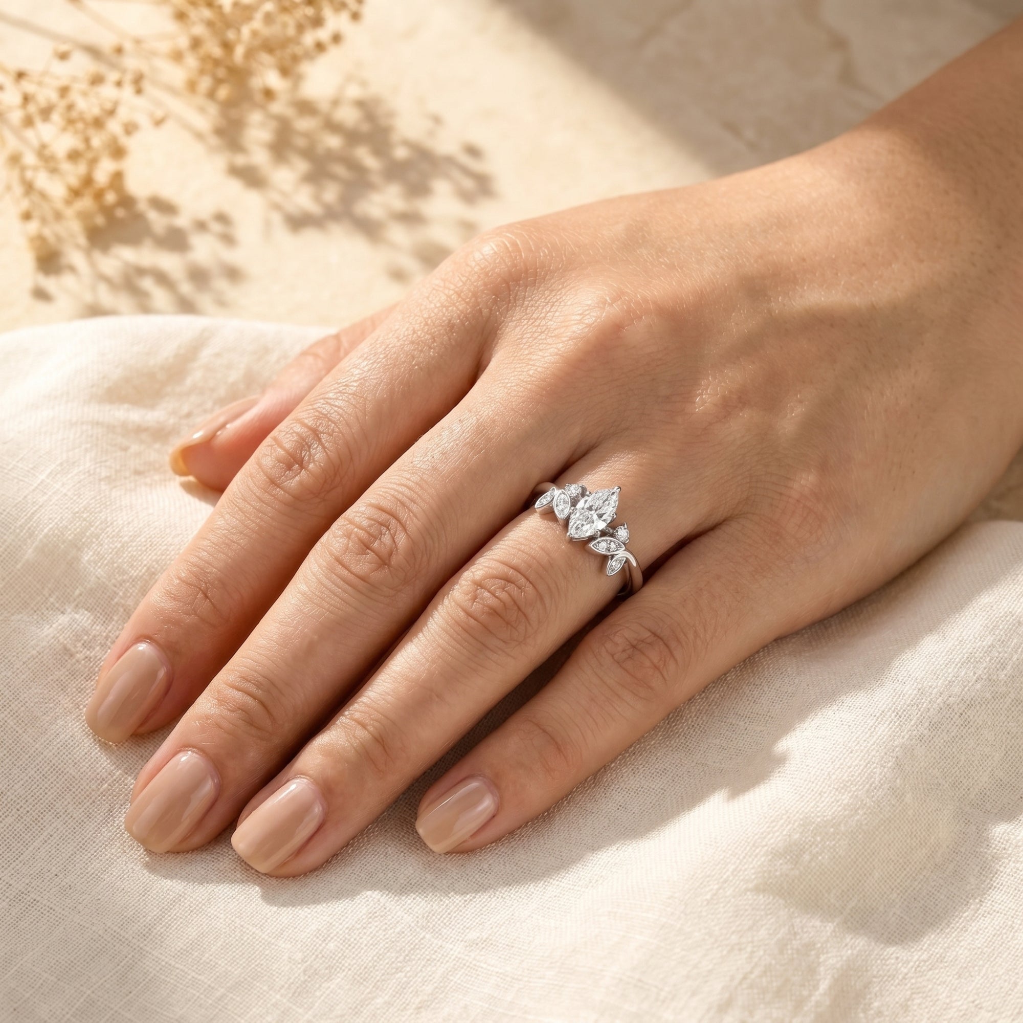 Marquise moissanite silver ring on a hand to show scale against white fabric.