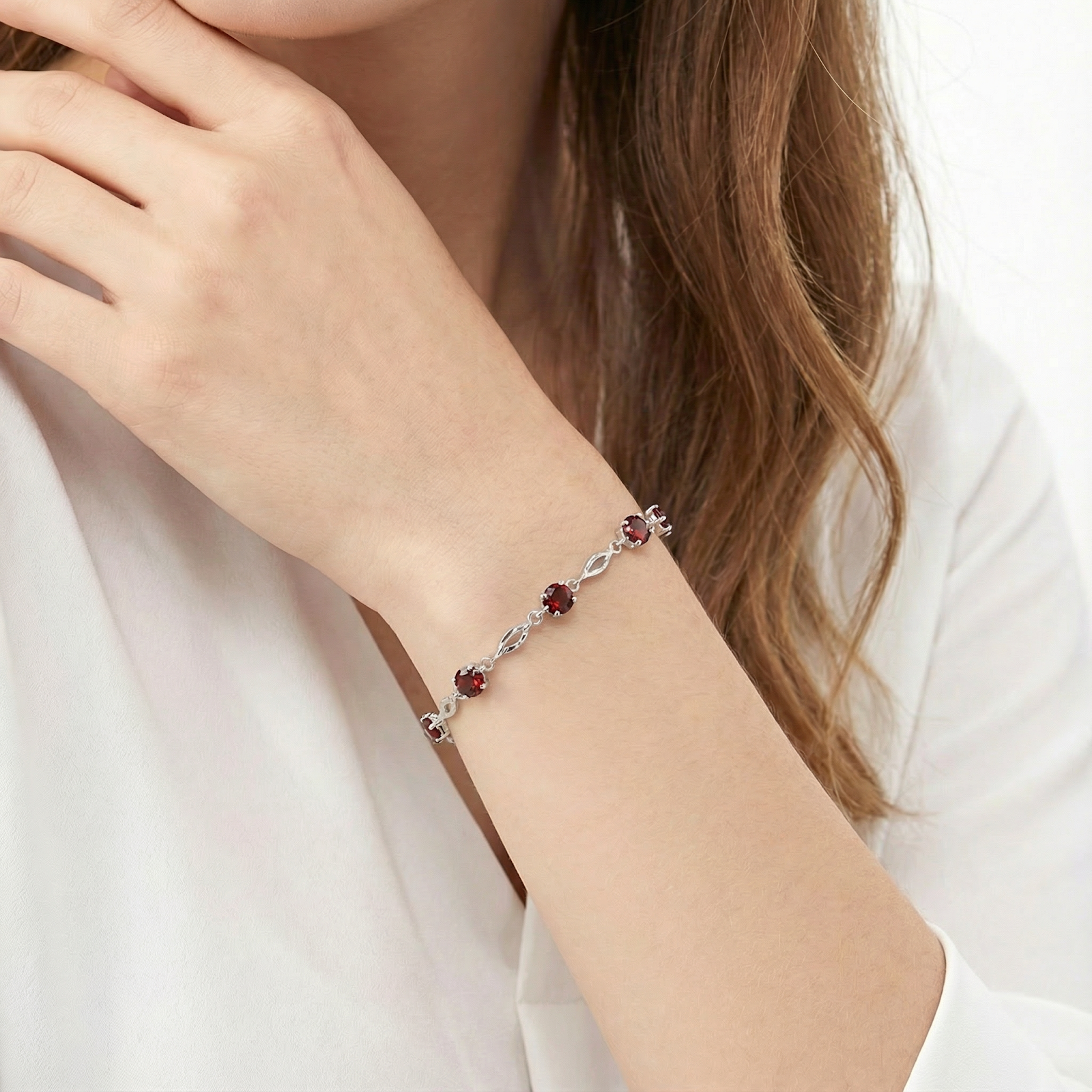 Close-up of the Eliora sterling silver station bracelet with round simulated garnets on a wrist.