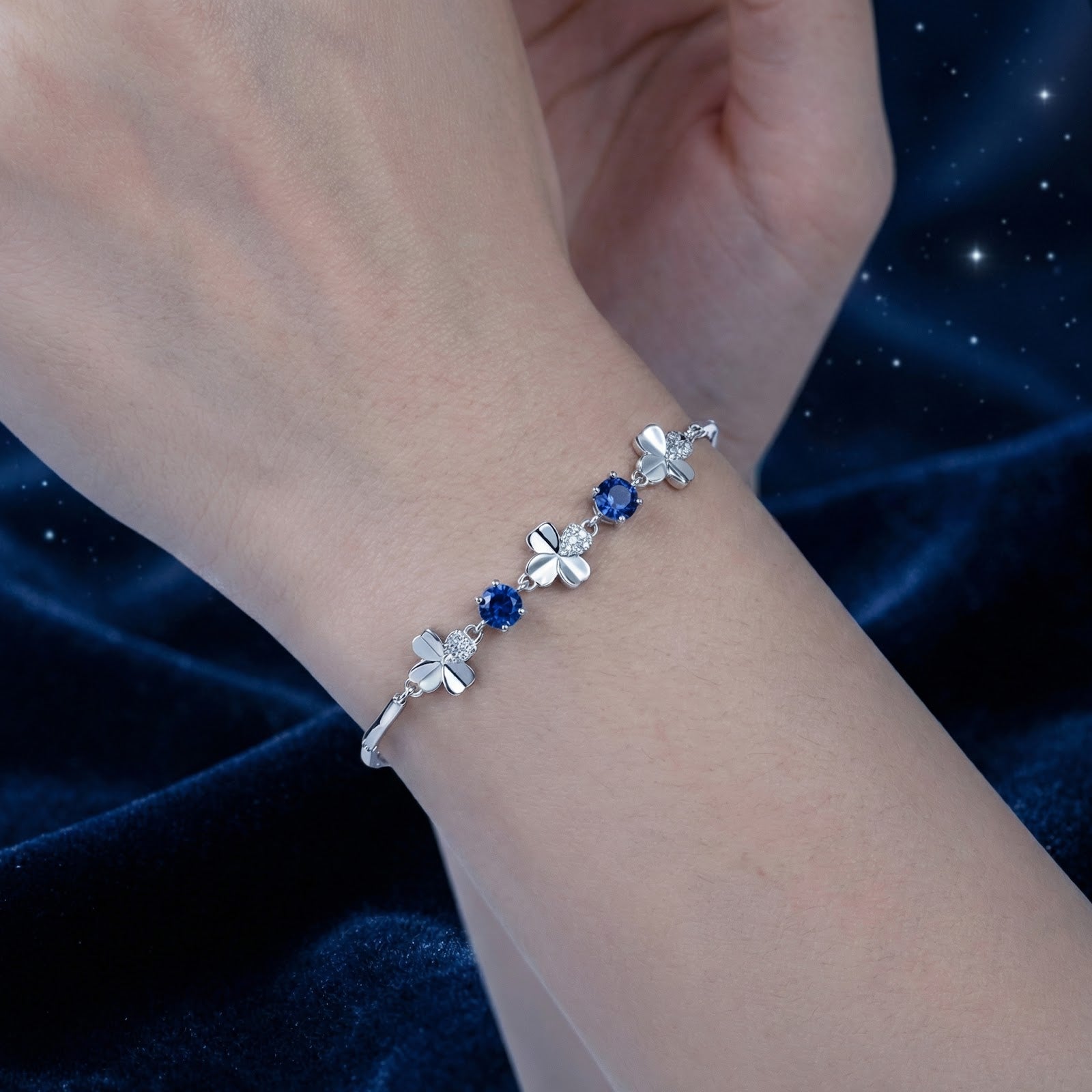 Detailed view of the silver clover and blue sapphire bracelet worn on a woman's wrist.