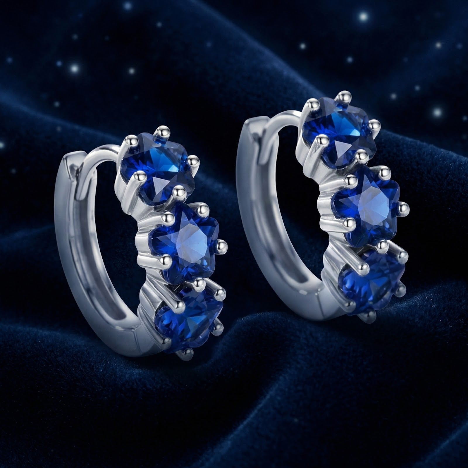 Angled view of sterling silver star huggie earrings with star-cut royal blue simulated sapphires on velvet.