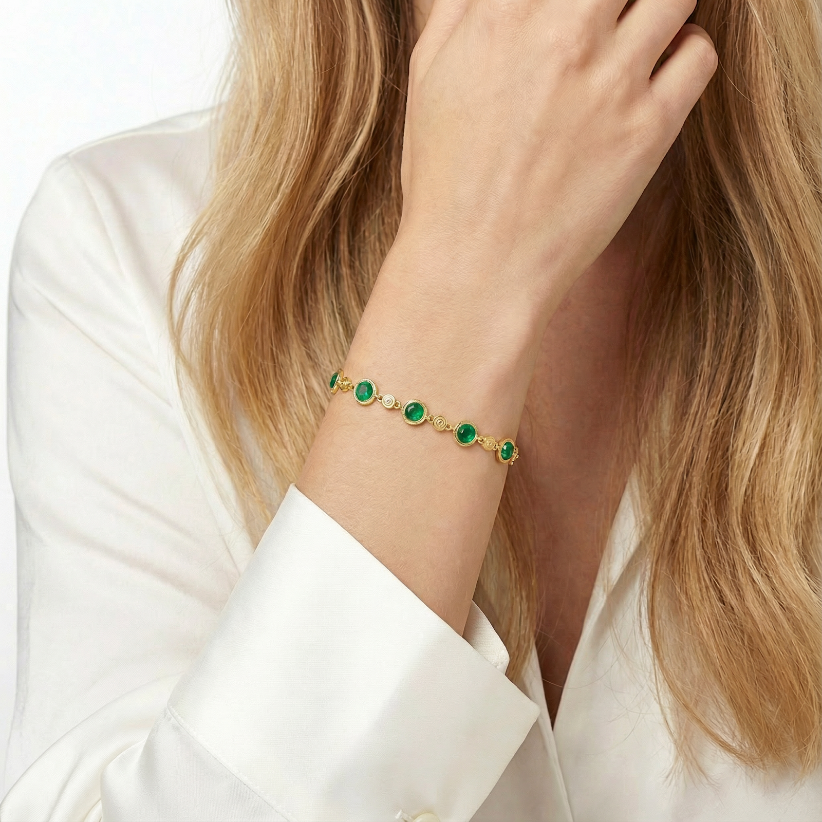Gold vermeil station bracelet with round green emerald stones worn on a woman's wrist with a white silk blouse.