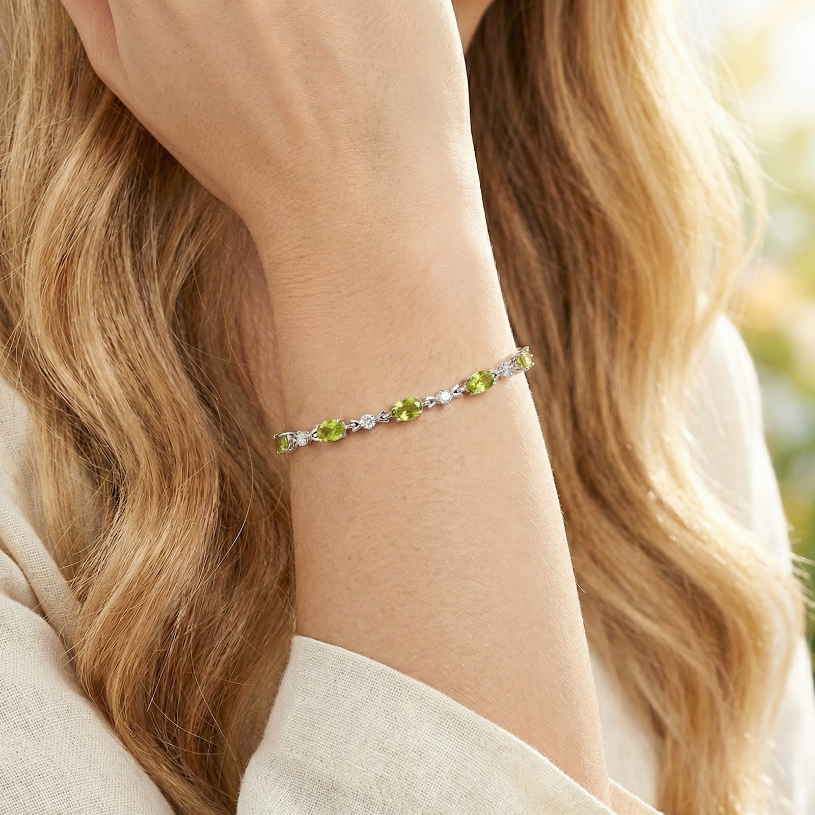Oval peridot tennis bracelet in silver worn on a woman's wrist, showcasing its scale and appearance on skin.