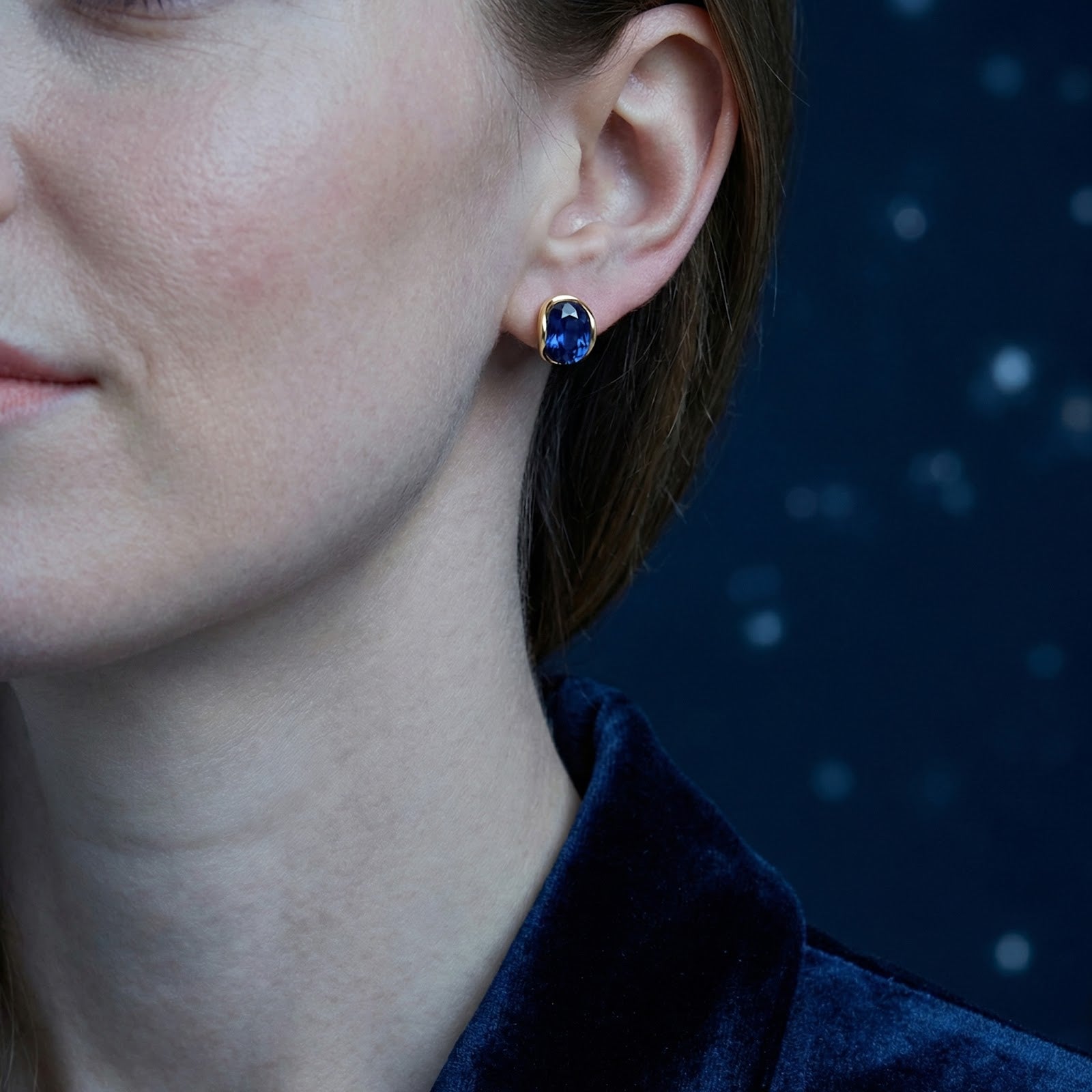Profile view of a model wearing the Seraphielle oval blue sapphire earrings in 18K gold vermeil.
