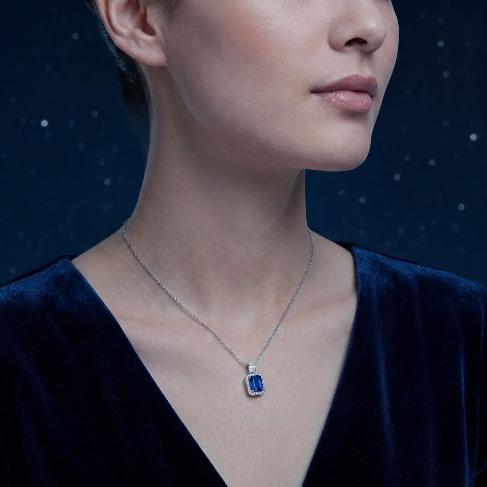 A woman wearing the emerald cut blue sapphire pendant in sterling silver, styled with a dark blue velvet dress.