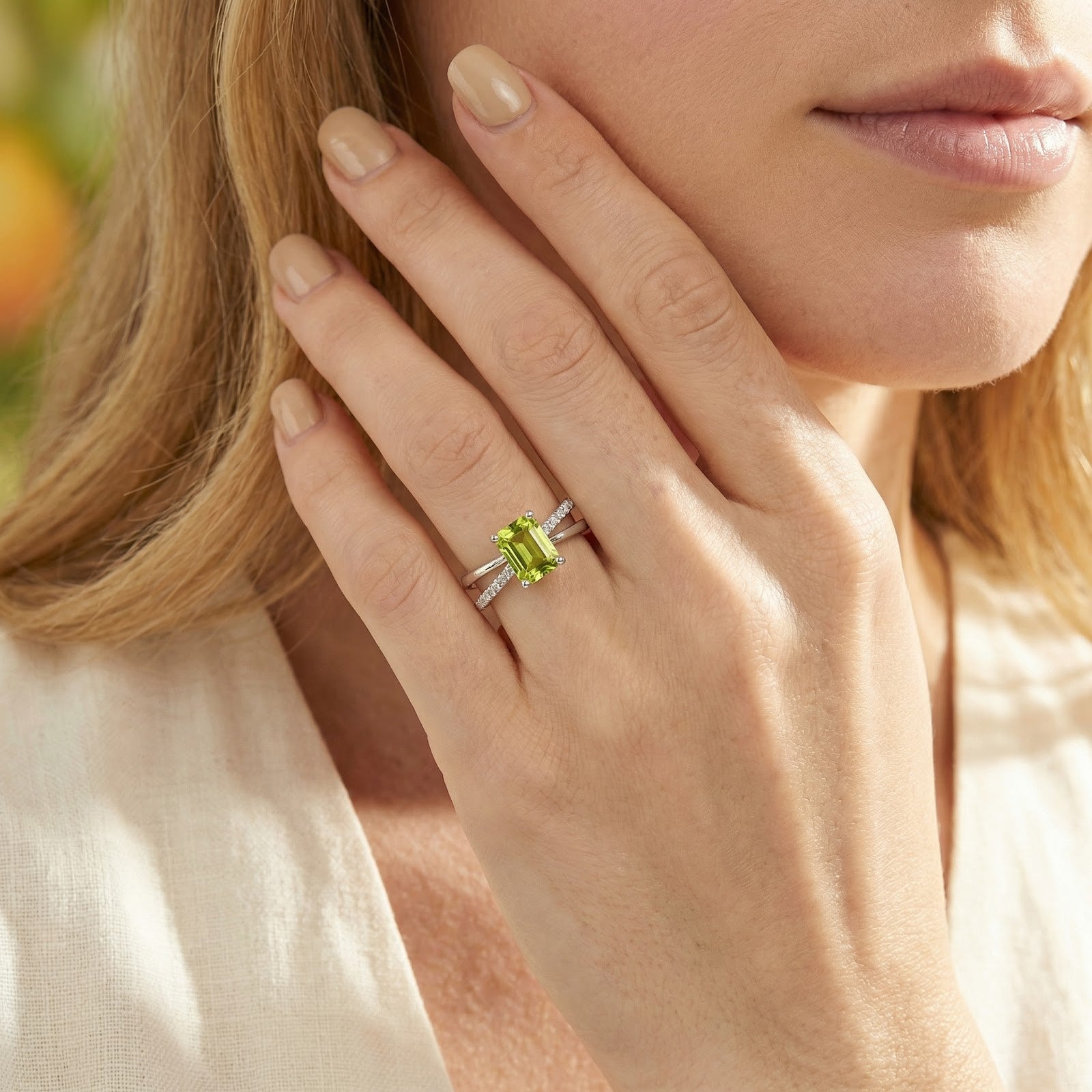 Close-up of a woman wearing the radiant cut simulated peridot sterling silver ring with a criss-cross band.