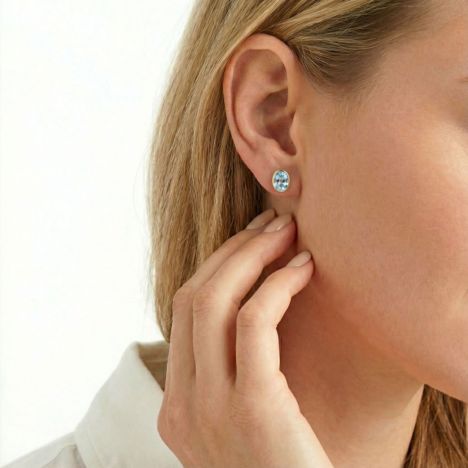 Oval cut light blue gemstone earring in a gold bezel setting worn on a model's ear.