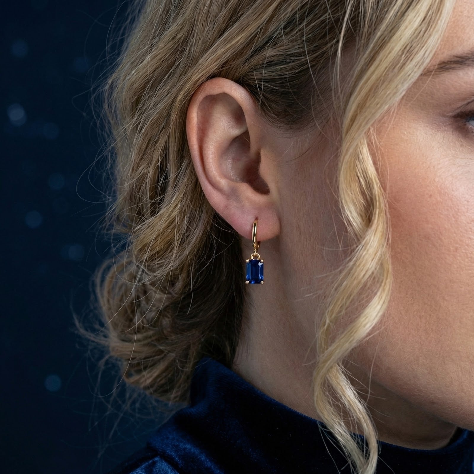 Woman wearing an 18K gold vermeil hoop earring with an emerald-cut simulated blue sapphire charm.