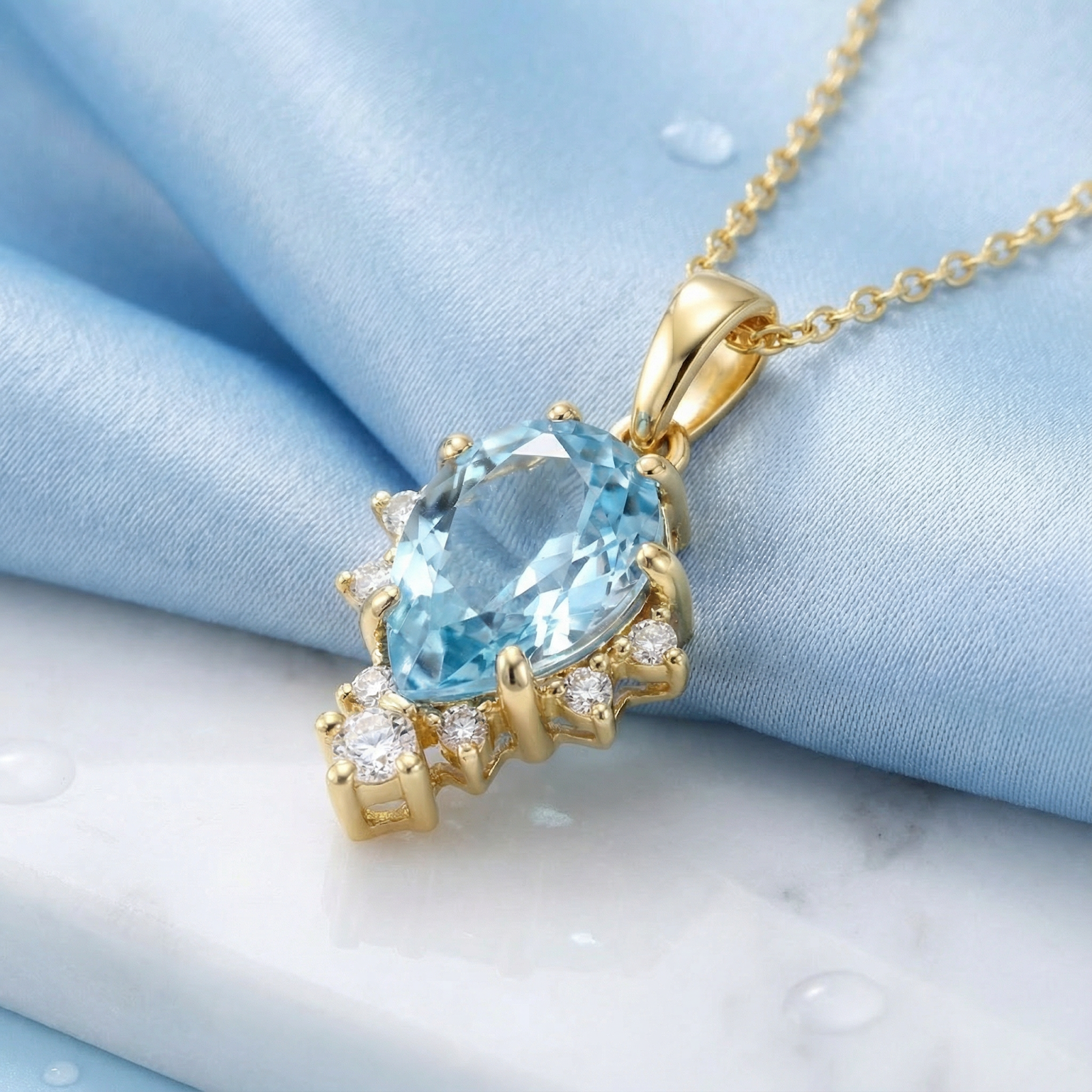 Pear cut simulated aquamarine necklace in 18K gold vermeil on blue silk with water droplets.
