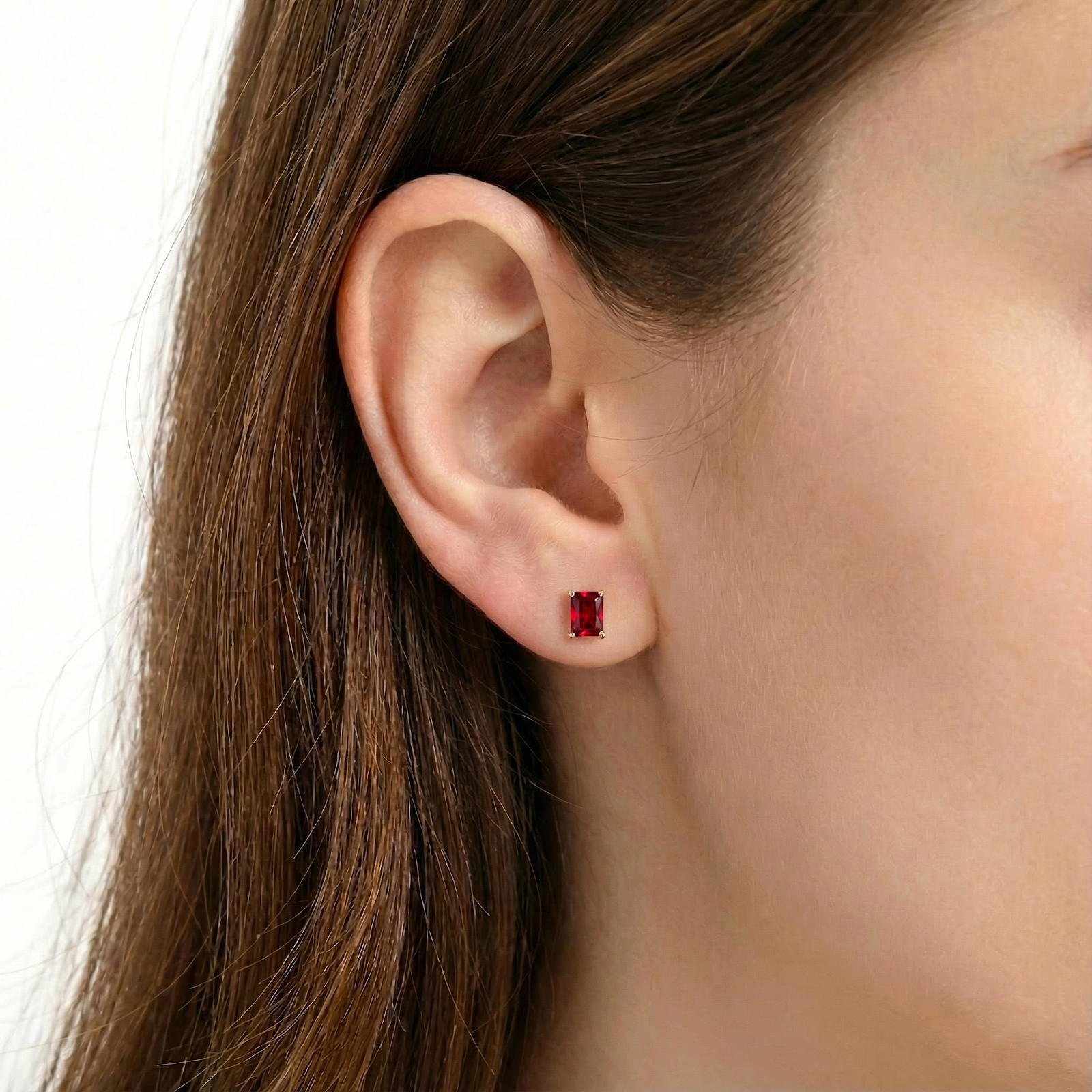 Woman wearing a Maricela emerald-cut simulated ruby stud earring in 18K gold vermeil.