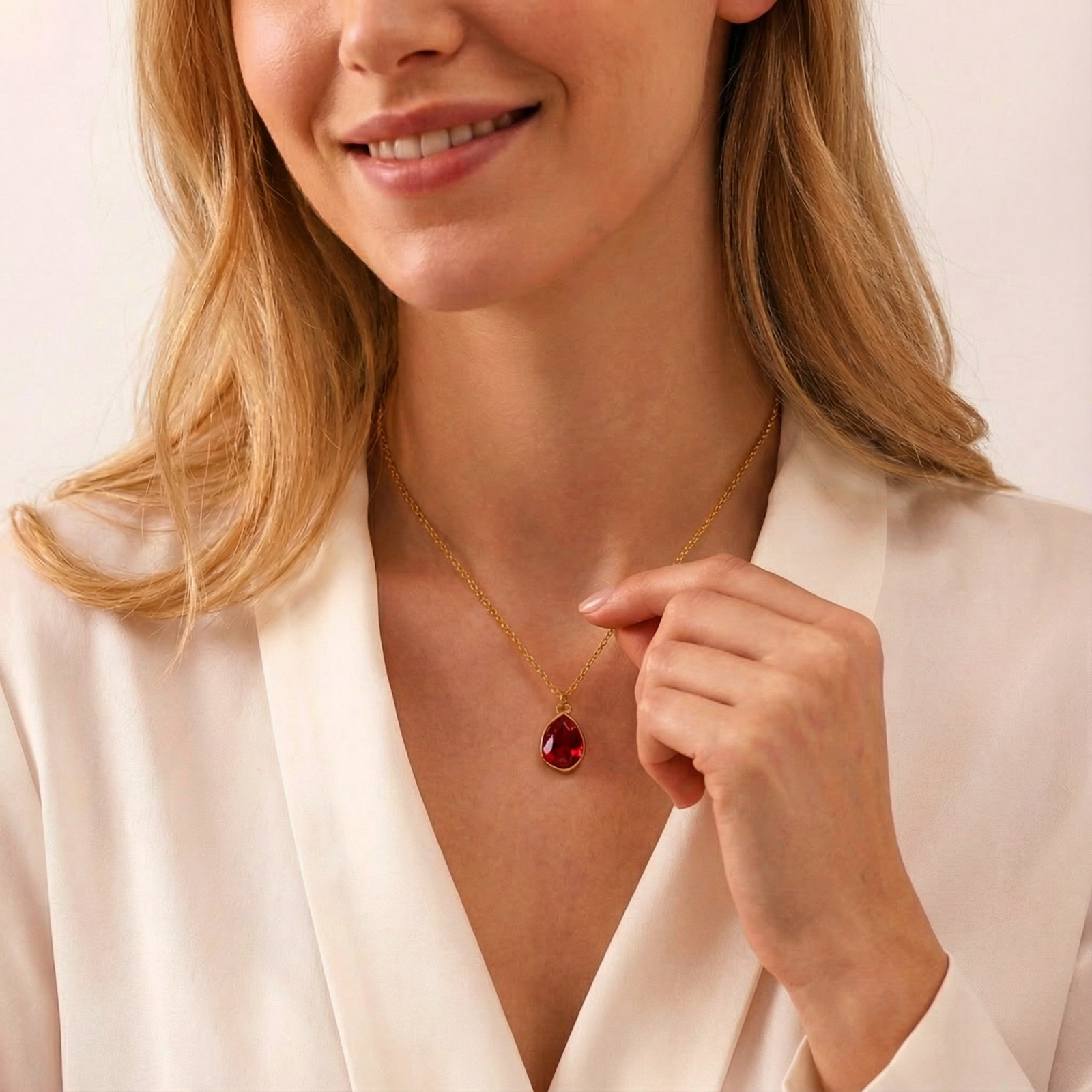A woman wearing the gold-toned July birthstone necklace with a red simulated ruby teardrop pendant.