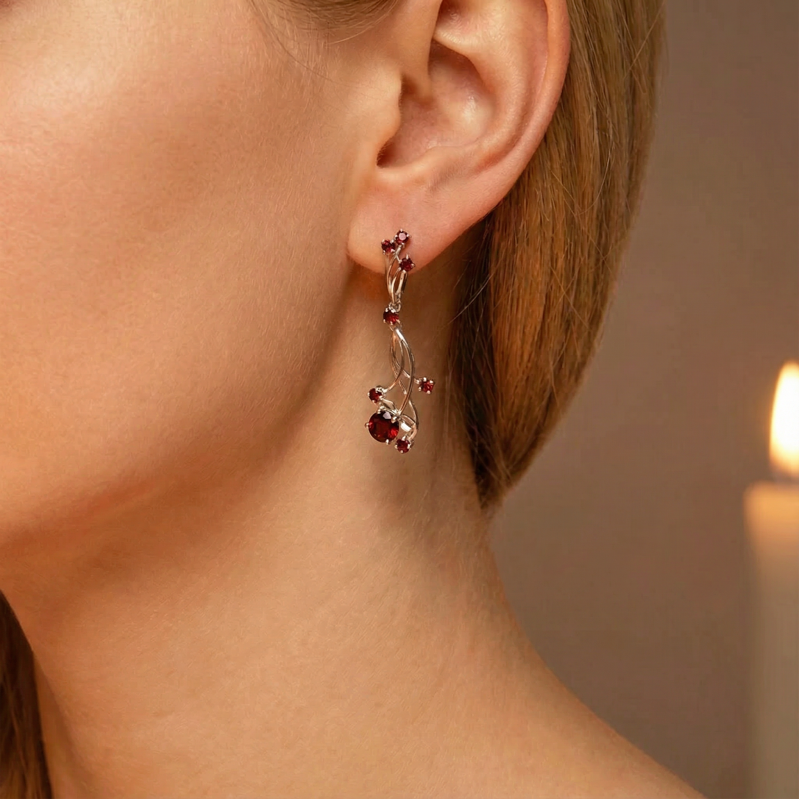Close-up of a red garnet and silver vine drop earring worn on a model's ear.