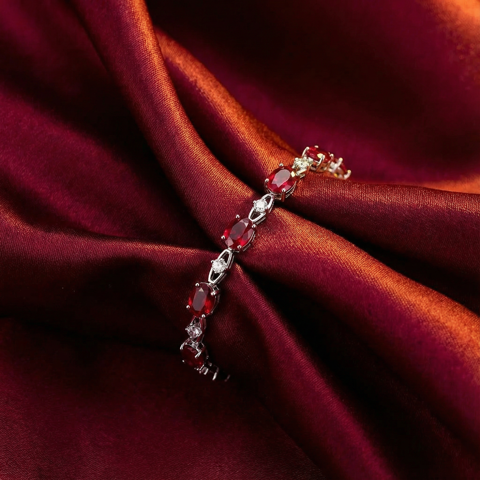 Sterling silver bracelet featuring oval-cut simulated rubies draped over elegant red satin fabric.