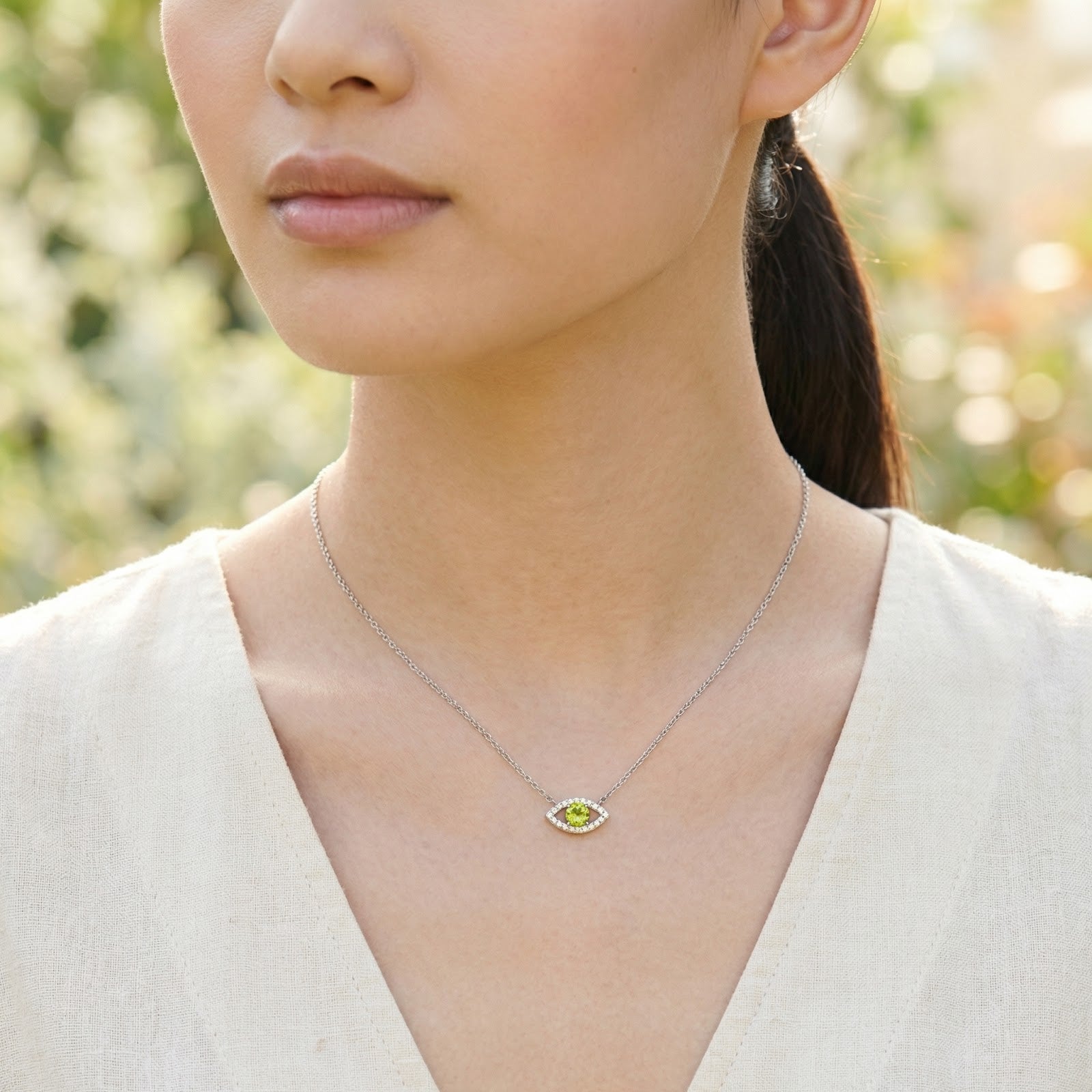 A woman wearing the silver eye motif necklace with a vibrant yellow-green round cut moissanite.