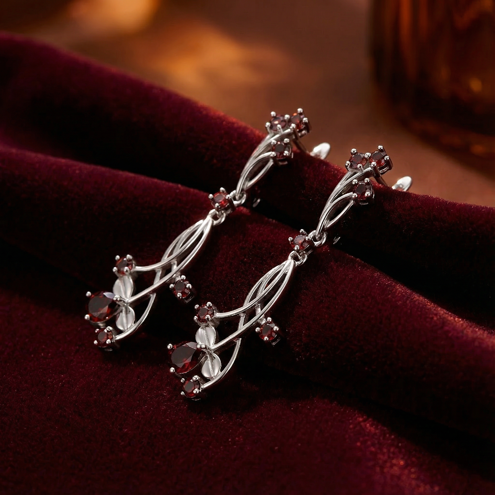Macro view of S925 sterling silver vine earrings with precision-cut round and pear red garnets.