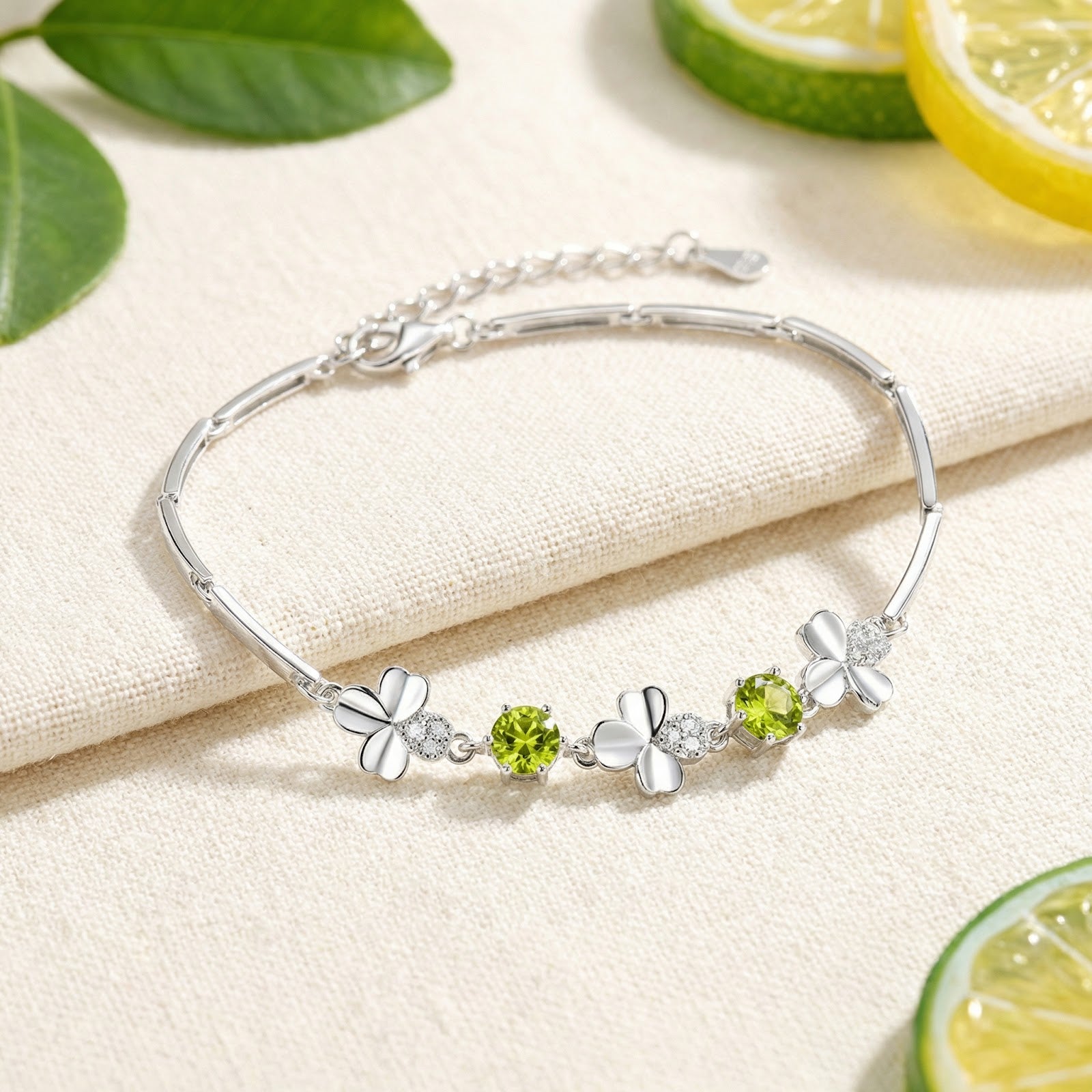 S925 sterling silver clover bracelet with round green peridot stones on a white surface with lemon slices.