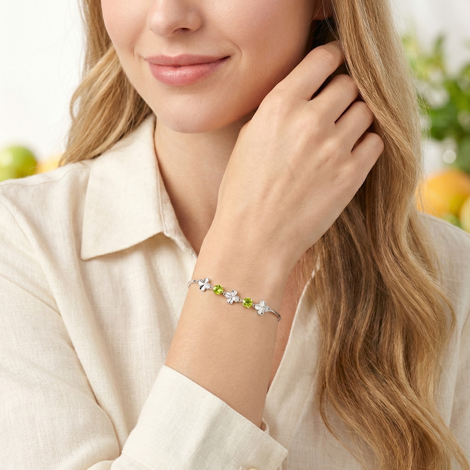 Woman wearing a beige linen shirt and the sterling silver clover bracelet with green peridot stones.