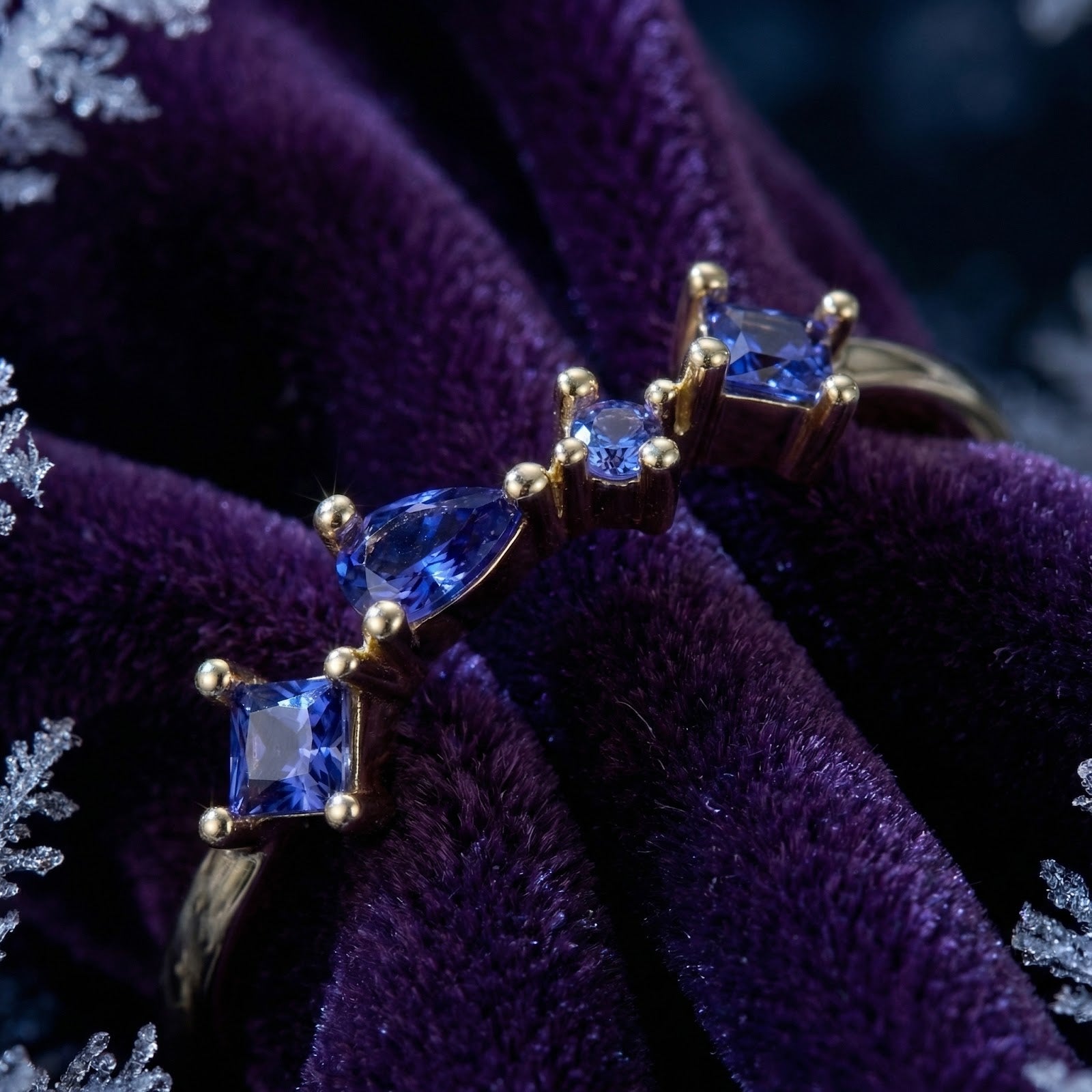 Macro shot of pear and princess cut simulated tanzanite stones in an 18K gold vermeil cascade ring on purple velvet.