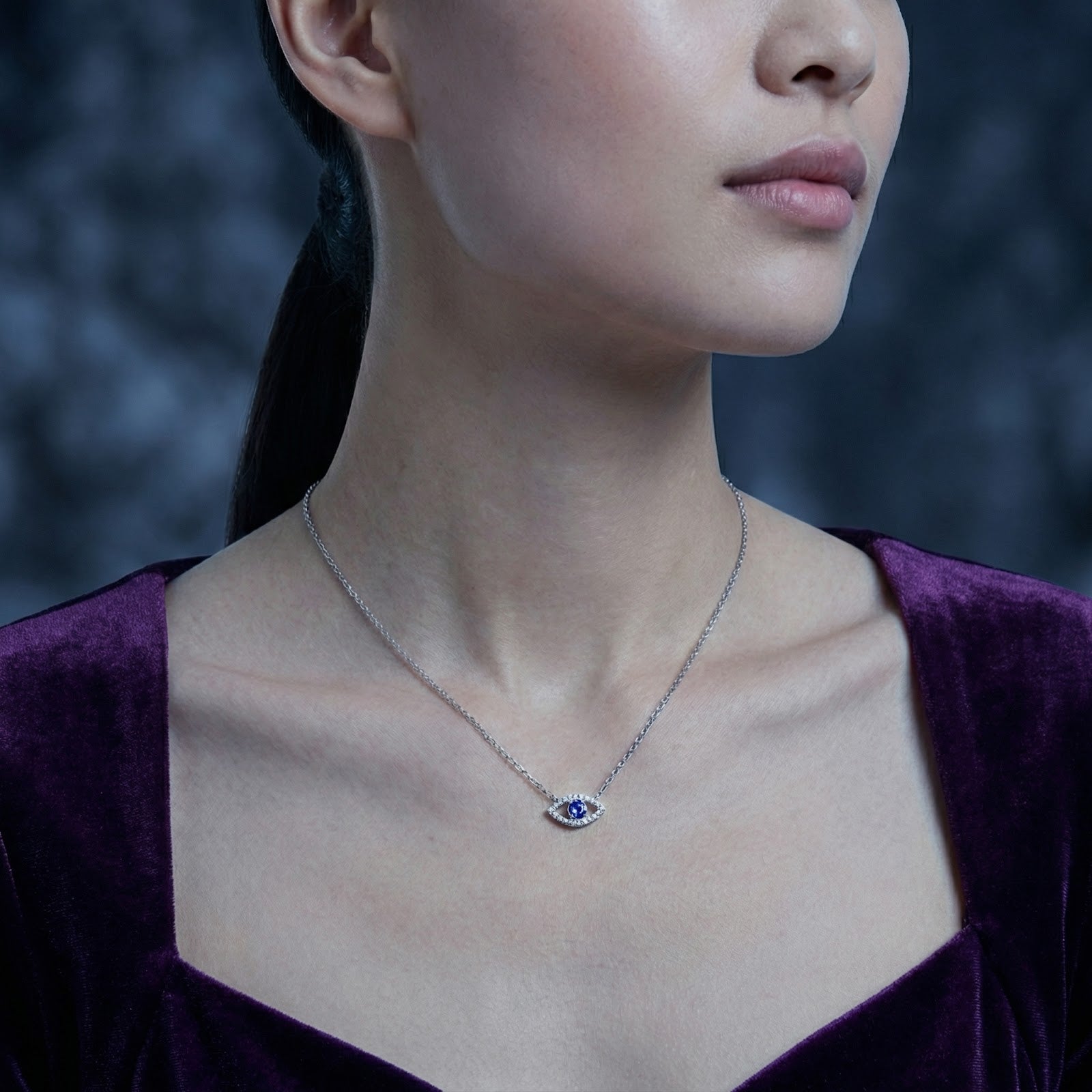 Silver Ismeria Eye necklace with simulated tanzanite worn by a model in a purple velvet dress.