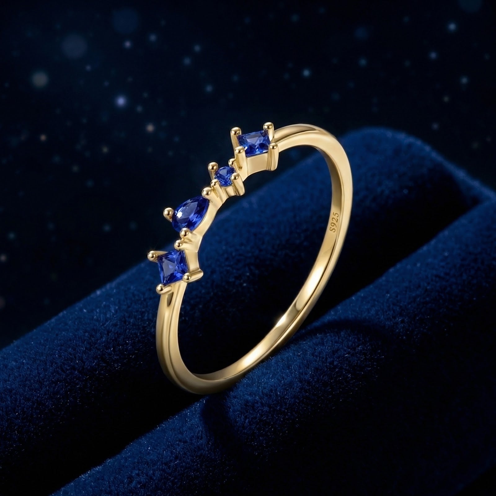 Nyara V-ring in 18K gold vermeil featuring pear, princess, and round cut simulated sapphires on blue velvet.