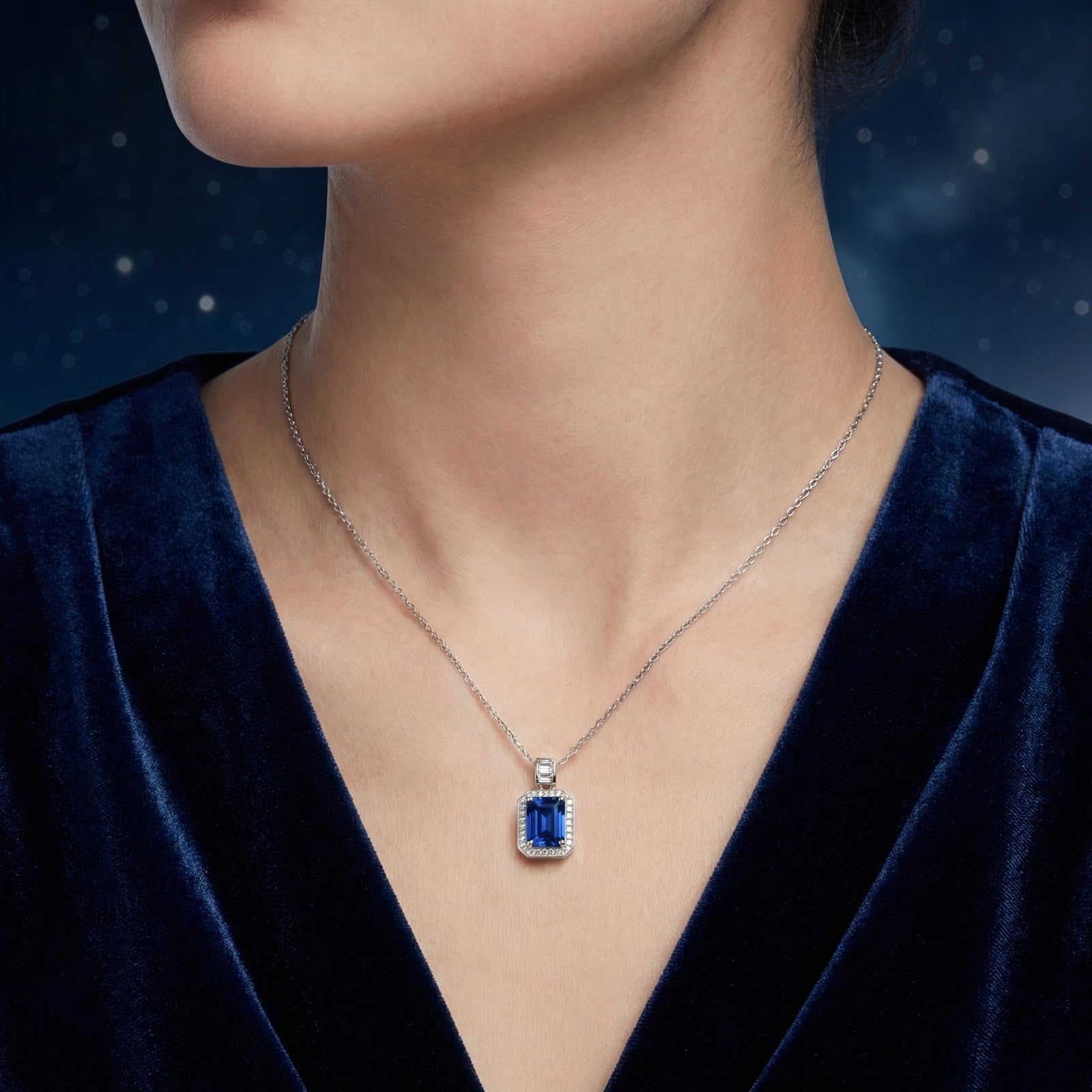 Model wearing the Rosamund emerald cut blue sapphire pendant on a silver chain against a starry backdrop.