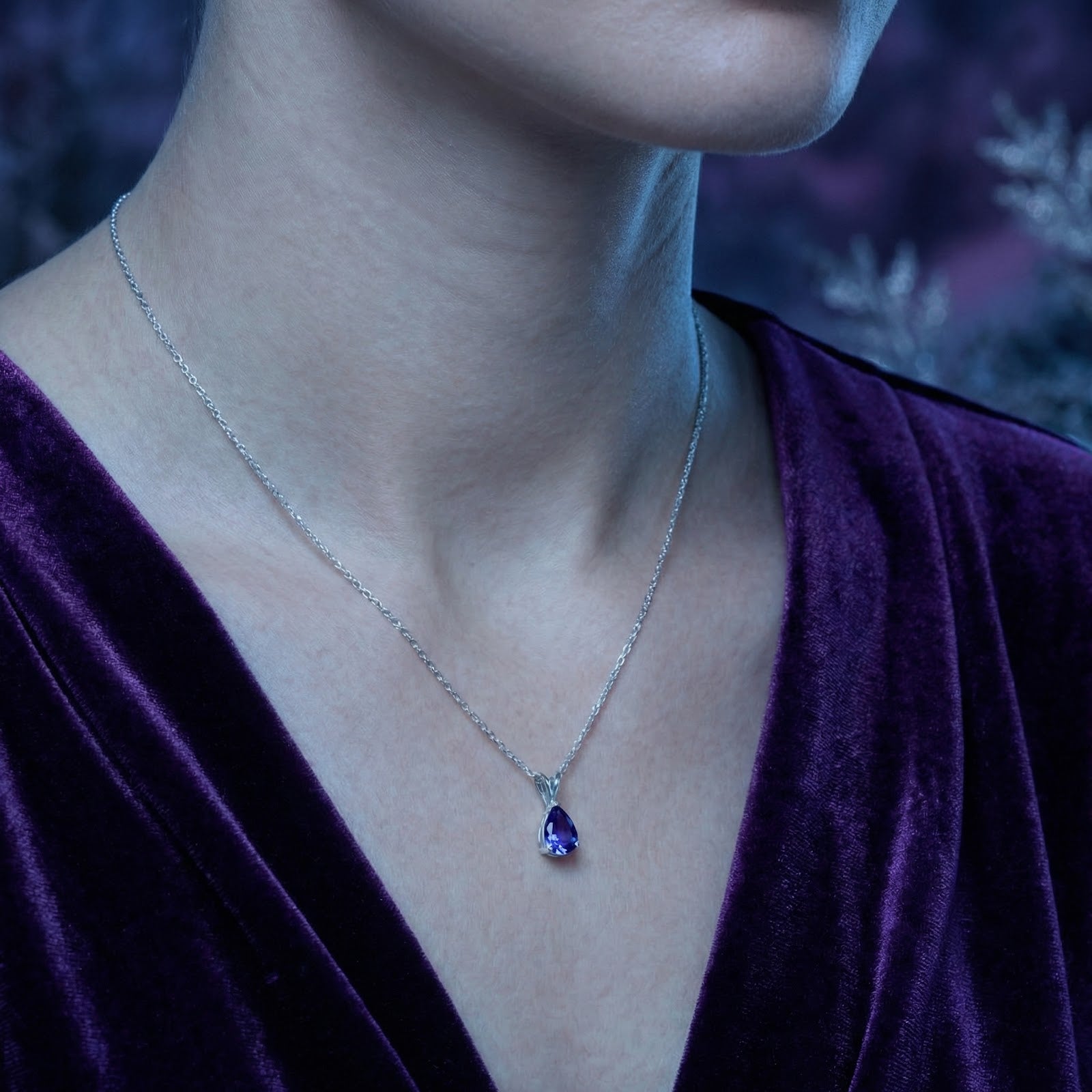 Silver necklace with a pear-cut blue moissanite pendant worn by a model in a purple velvet outfit.