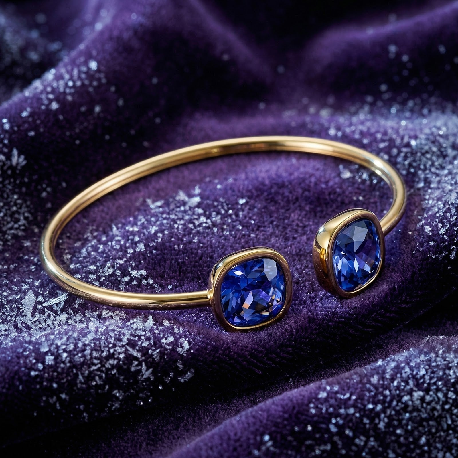Angled view of gold stainless steel Nerina bangle with cushion-cut simulated tanzanite stones on purple velvet.