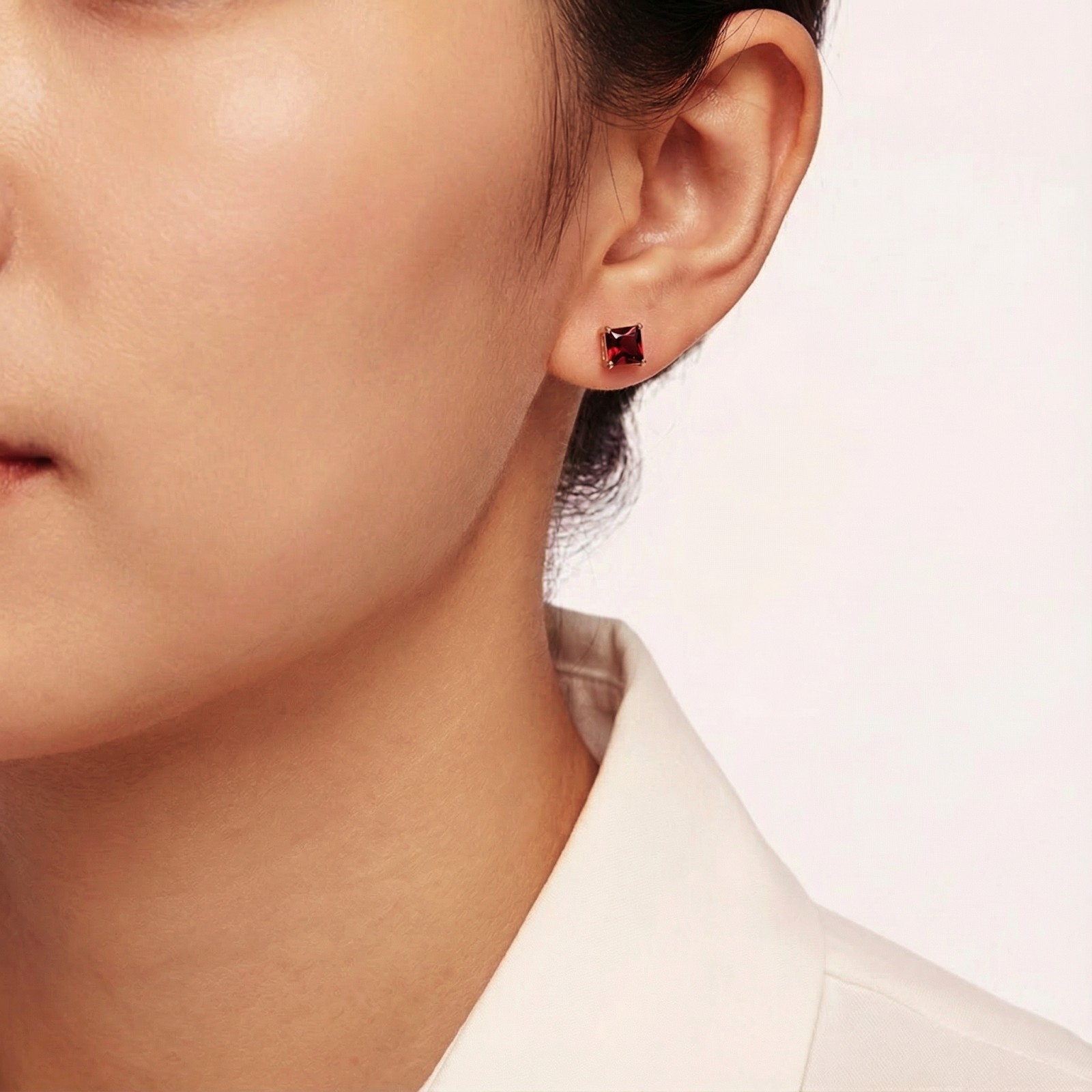 Woman wearing a square cut simulated garnet stud earring in 18K rose gold vermeil on her ear.