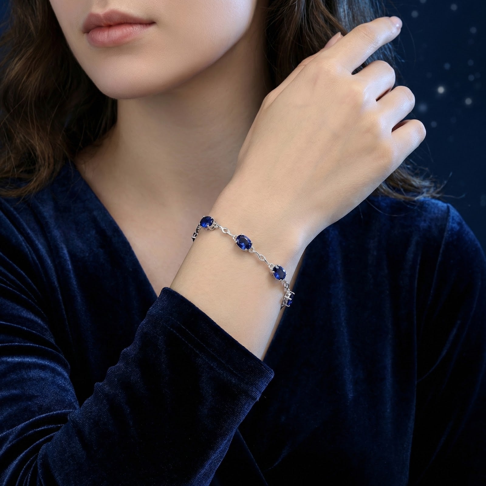 Adjustable sterling silver station bracelet with oval blue simulated sapphires worn on a woman's wrist.