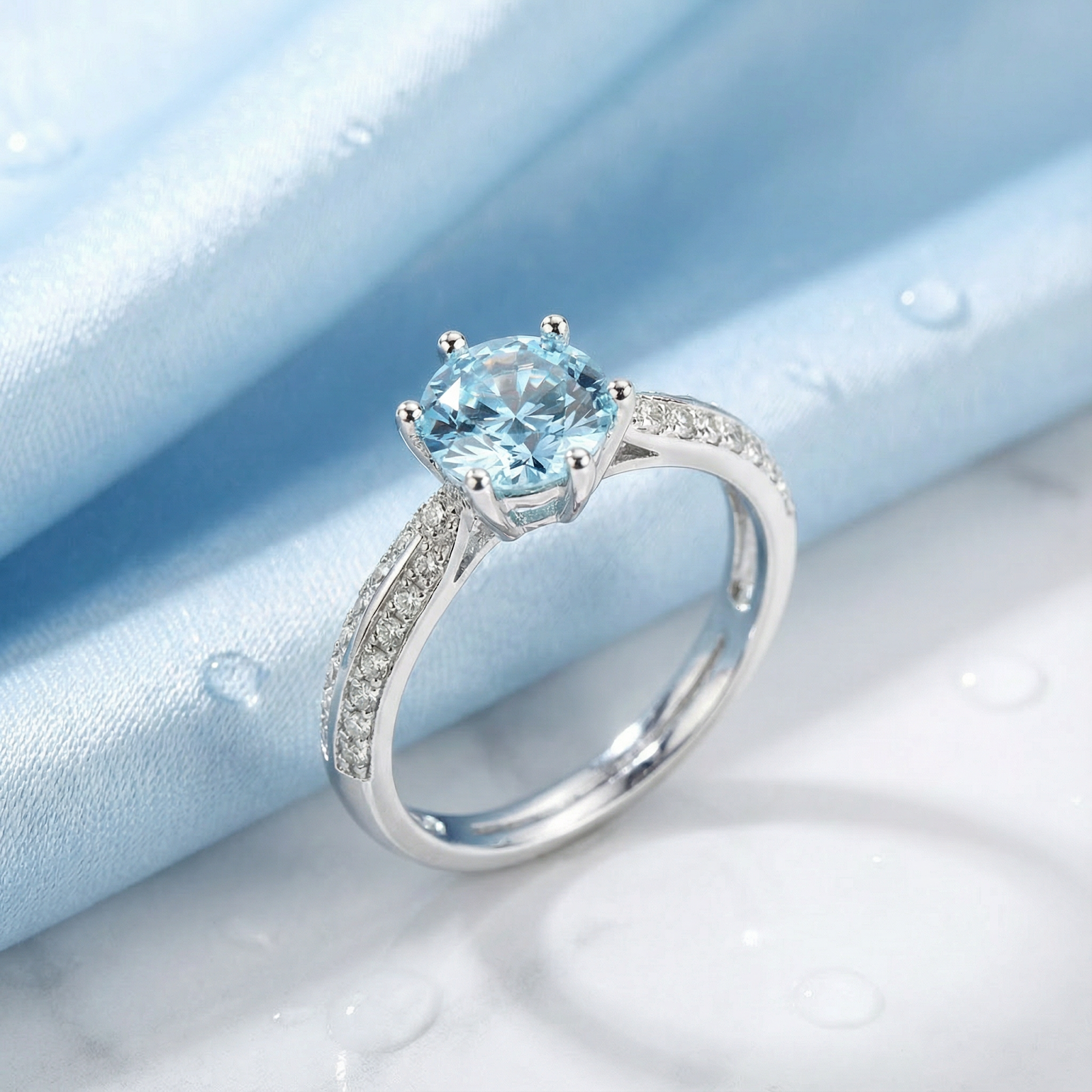 Round cut simulated aquamarine solitaire ring in S925 sterling silver on a light blue silk background.
