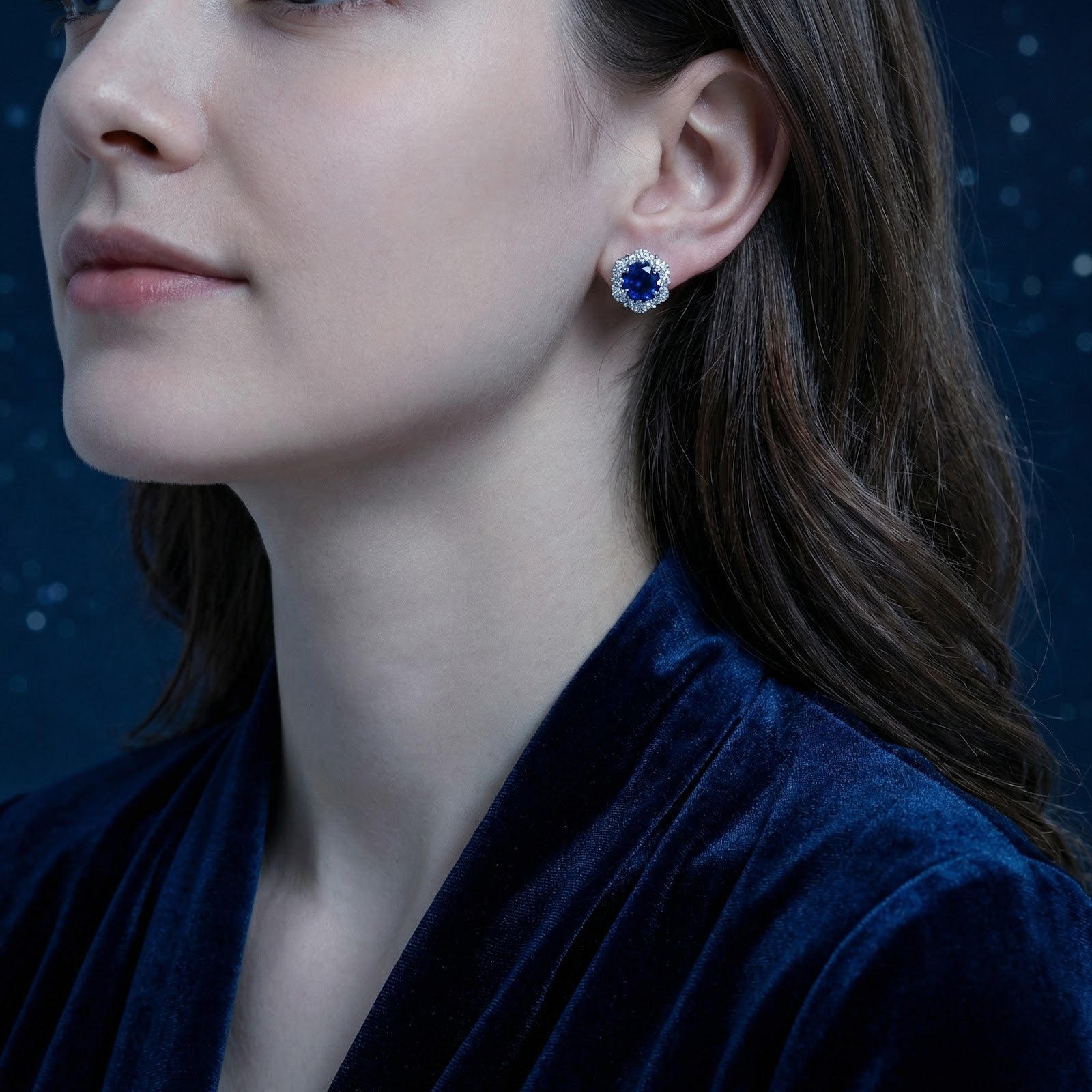 Side profile of a woman wearing the Serenis blue simulated sapphire halo stud earrings in sterling silver.