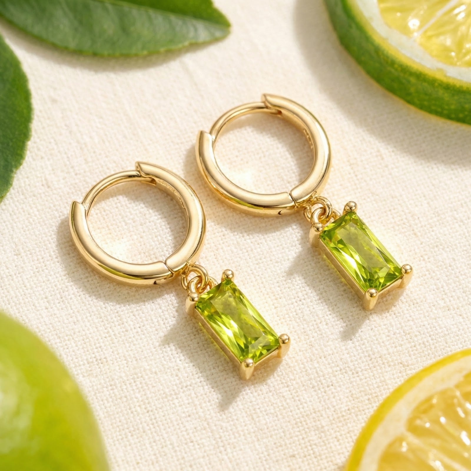 18K gold vermeil Lunaris hoop earrings with emerald-cut simulated peridot drops on a lifestyle lime slice background.
