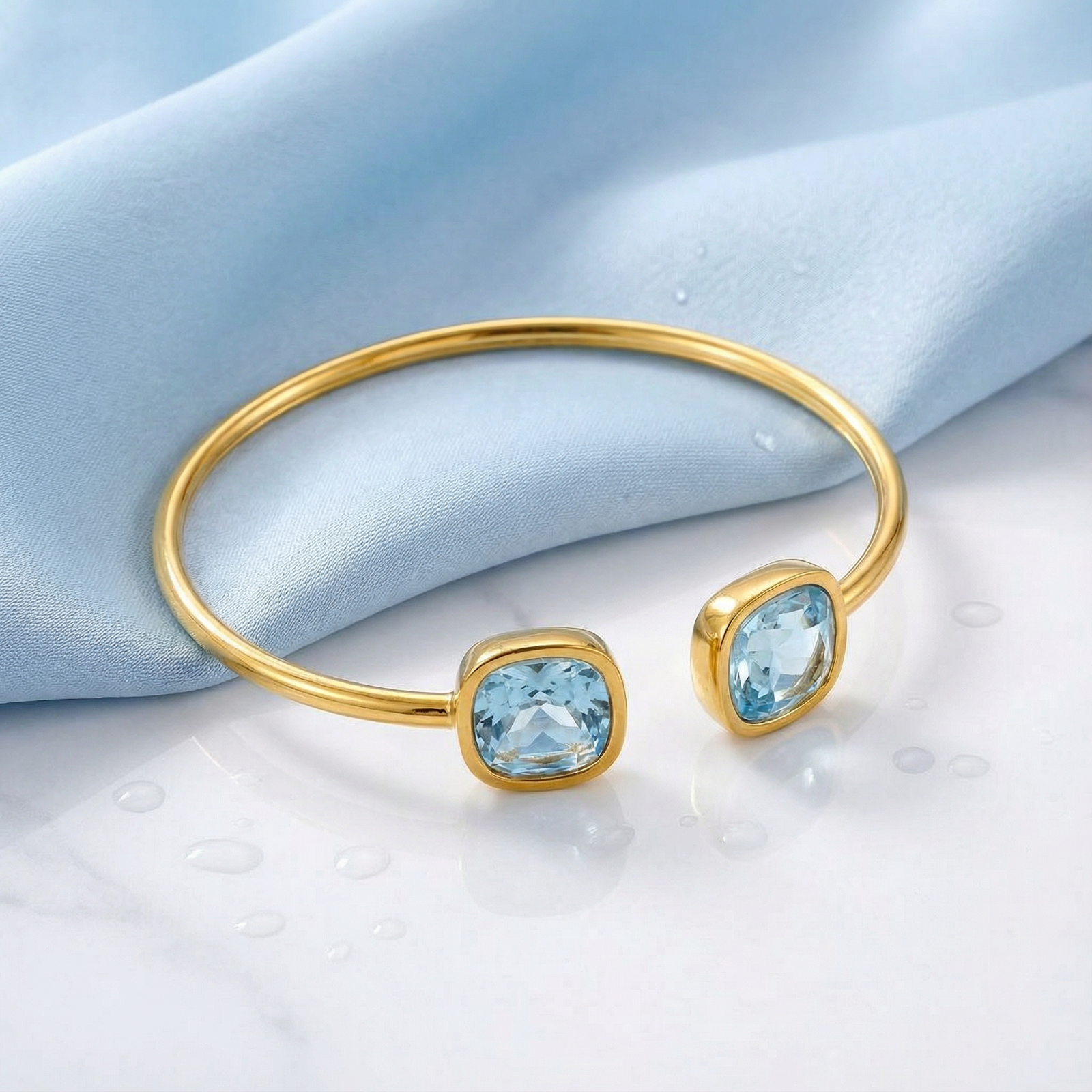 Gold stainless steel March birthstone bypass cuff with two cushion-cut simulated aquamarine stones.