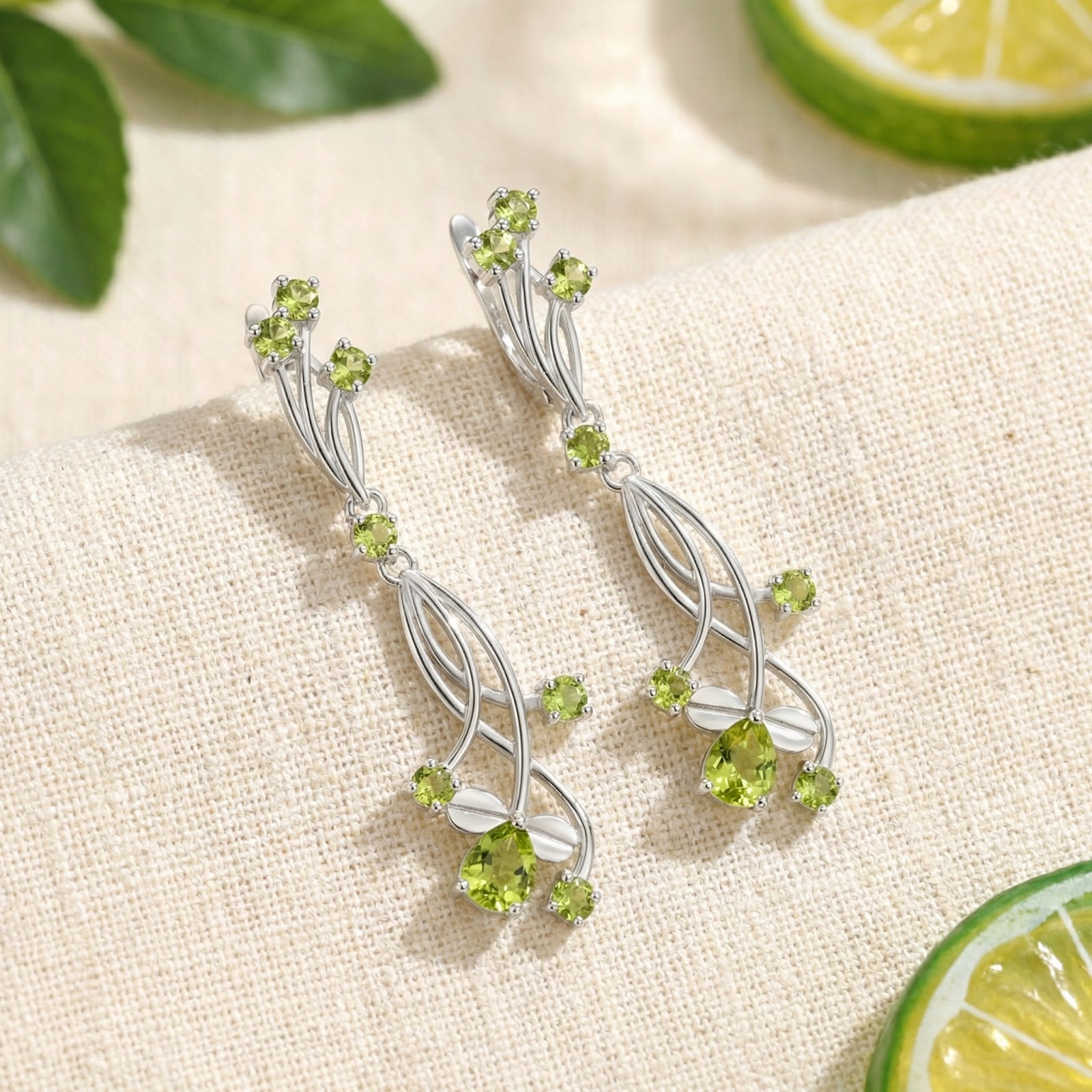 Sterling silver vine drop earrings with pear and round-cut simulated peridot on white fabric with lime accents.
