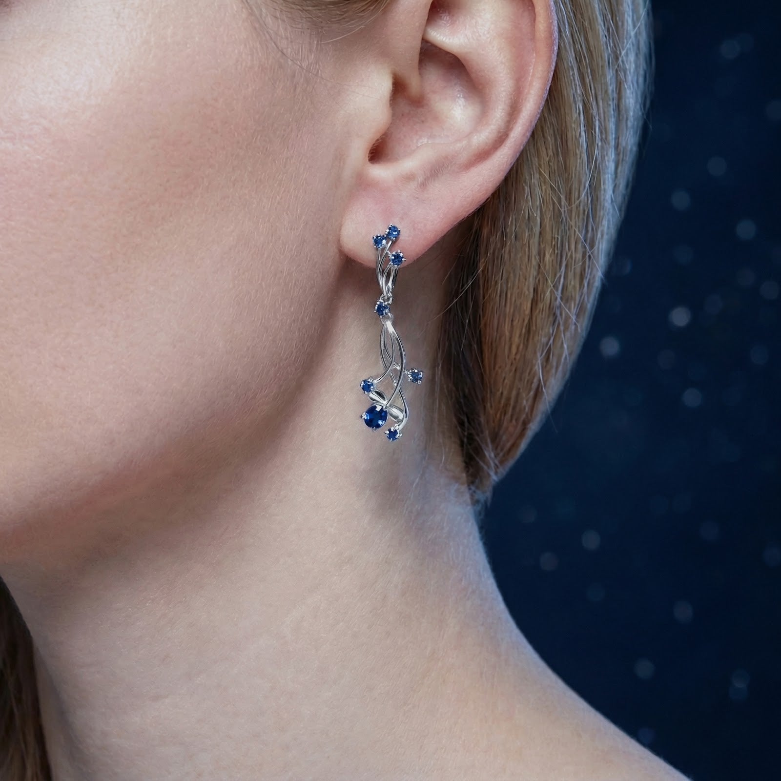 Close-up of a sterling silver vine drop earring with blue simulated sapphires worn on a model's ear.