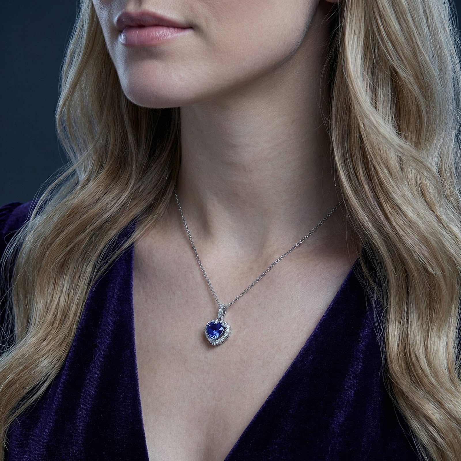 Angled view of a model wearing a heart-shaped blue tanzanite halo necklace in S925 sterling silver.
