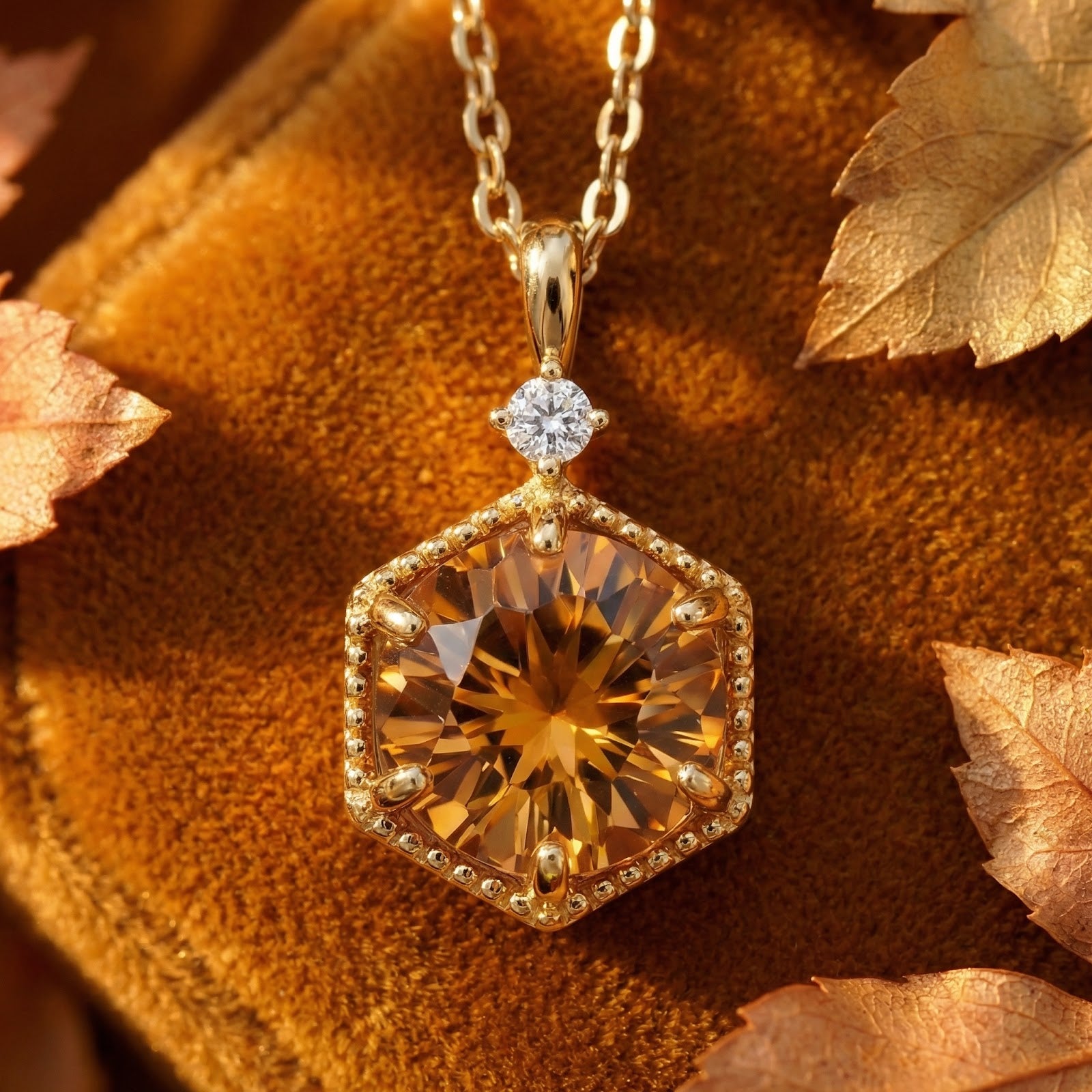 Hexagon-cut simulated topaz pendant in 18K gold vermeil on a brown velvet surface with autumn leaves.