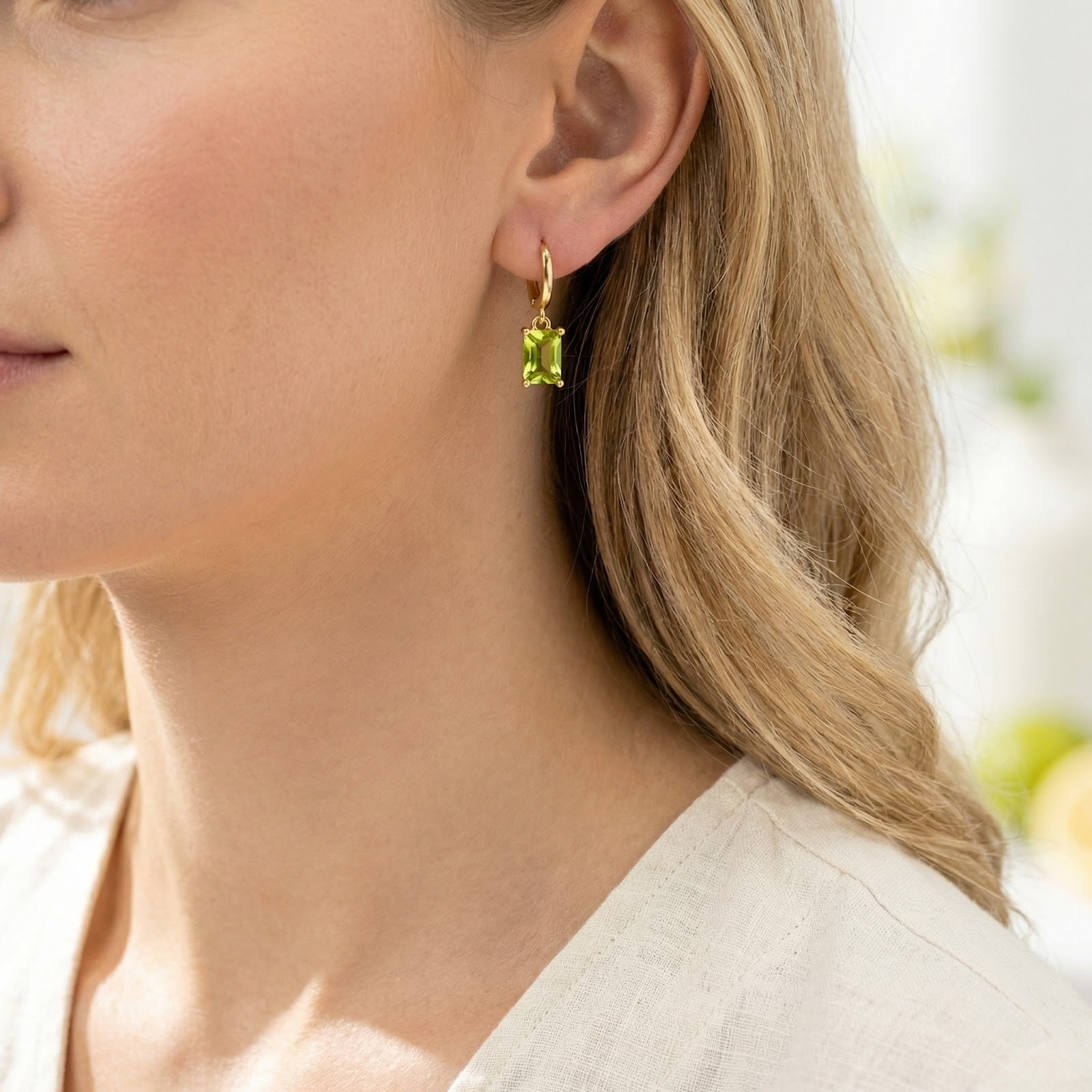 Close-up of a model wearing a gold vermeil Lunaris earring with a vibrant emerald-cut simulated peridot drop.