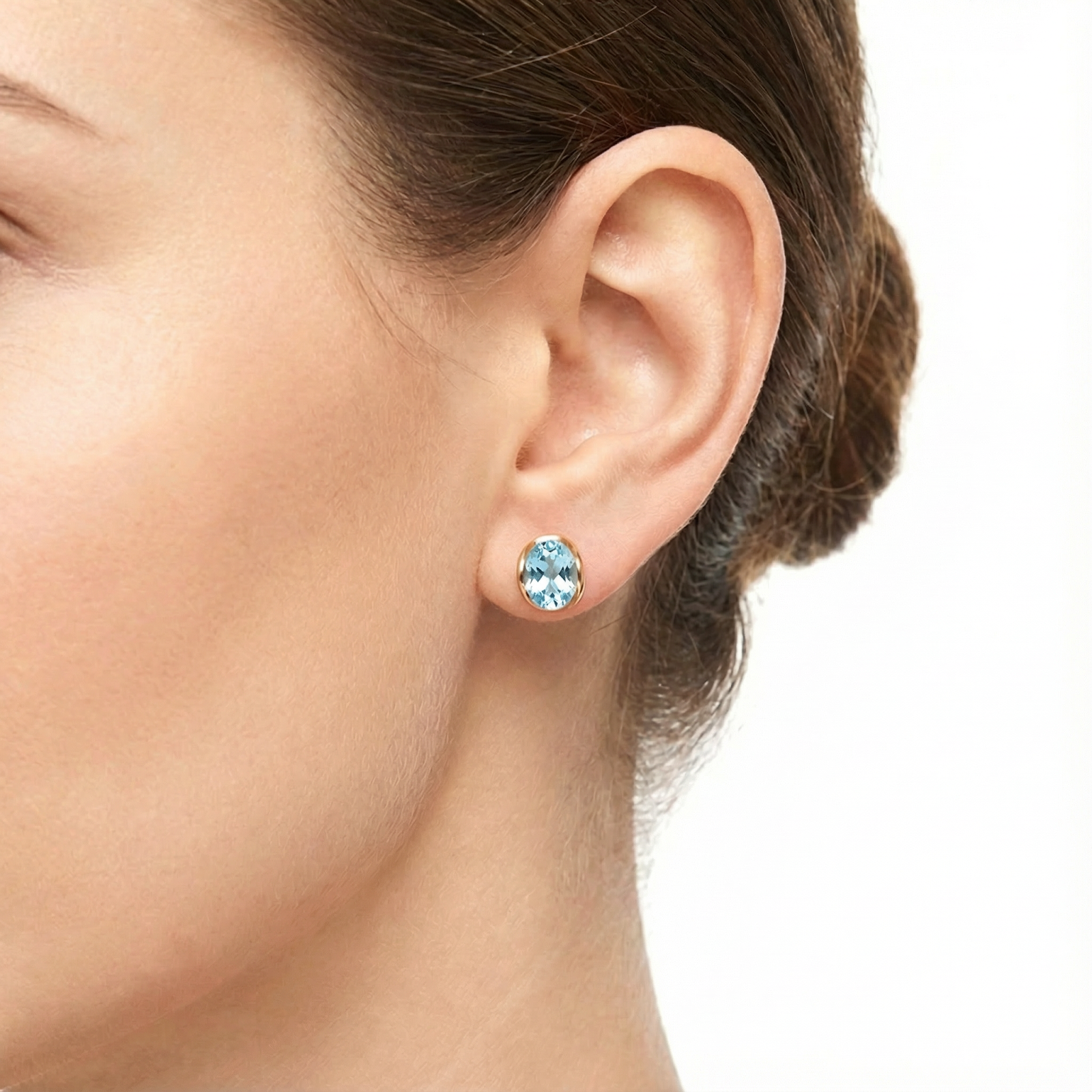 Close-up of a model's ear wearing an 18K gold vermeil huggie earring with an oval-cut simulated aquamarine stone.