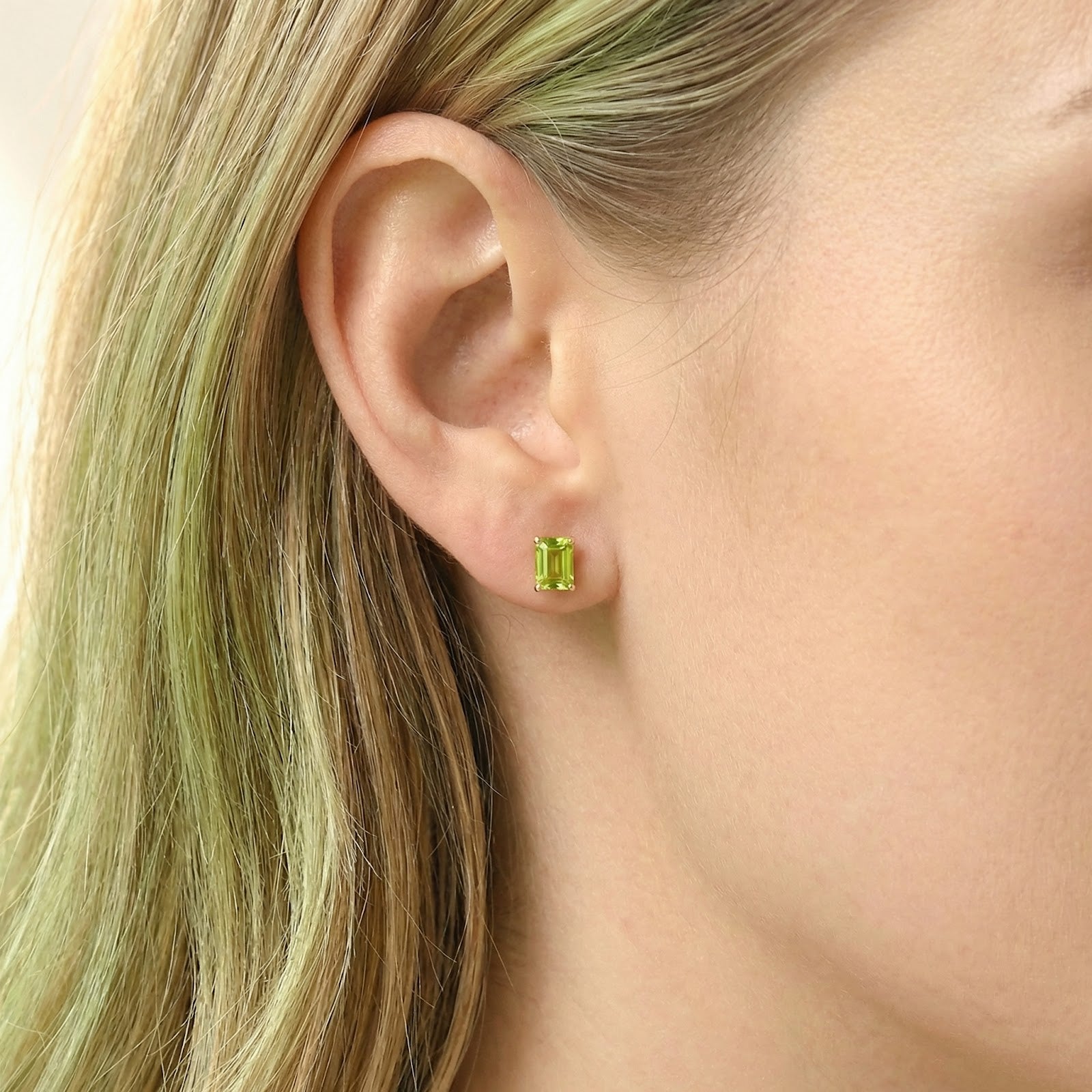 Woman with blonde hair wearing an emerald cut simulated peridot stud earring in 18K gold vermeil.