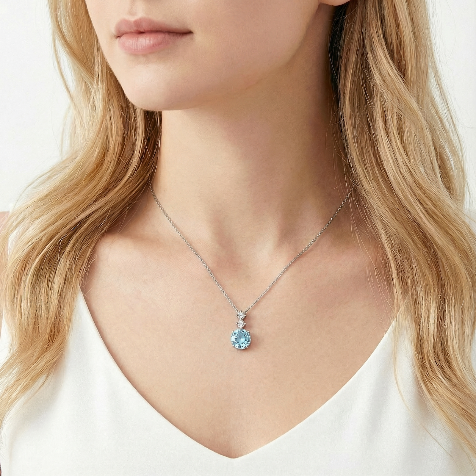 Sterling silver necklace with a round-cut simulated aquamarine pendant worn by a model in a white blouse.
