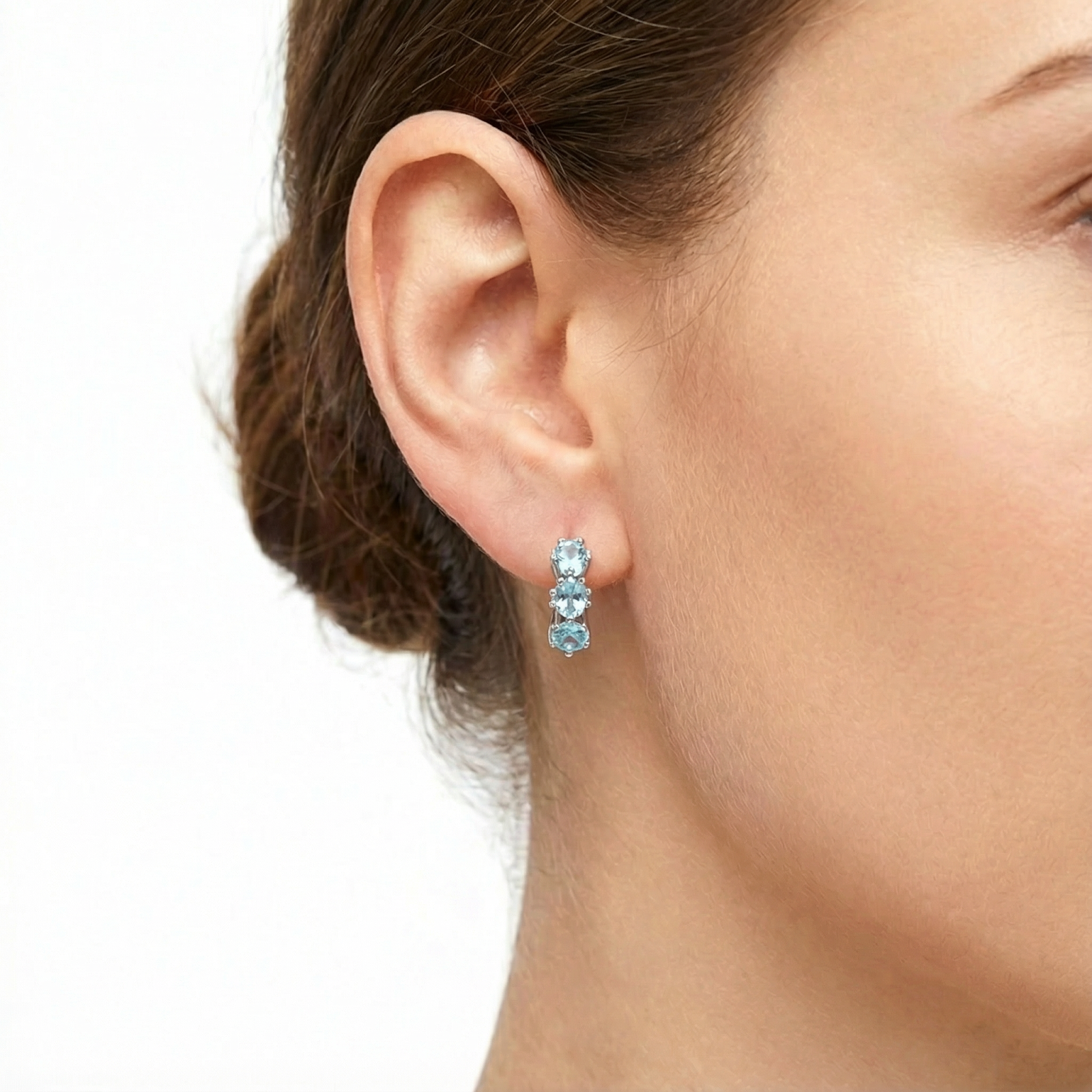 Close-up of a woman wearing a sterling silver Astra Star Hoop earring with three star-cut light blue aquamarine stones.