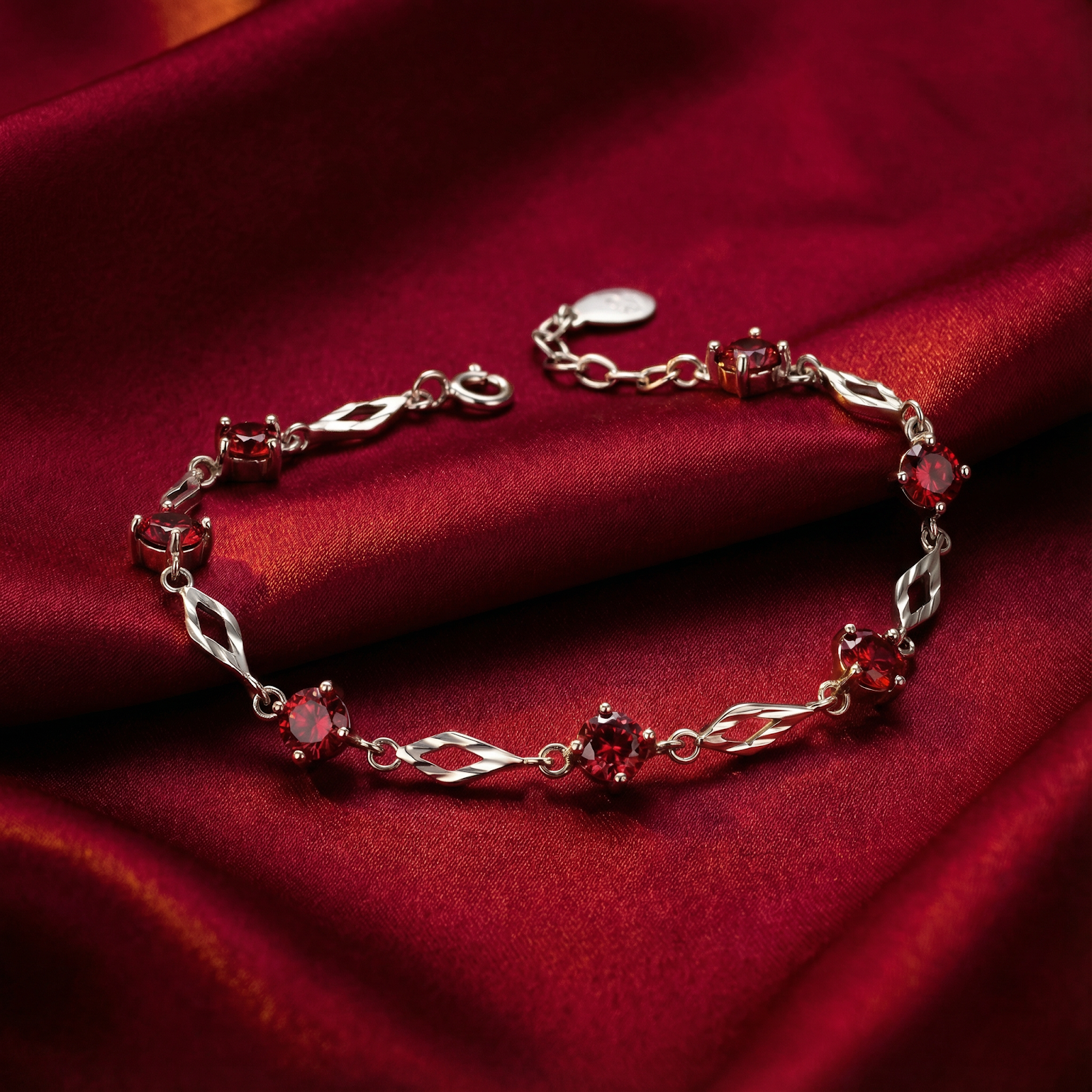 Aderyn station bracelet in S925 sterling silver with round-cut simulated rubies on red silk background.