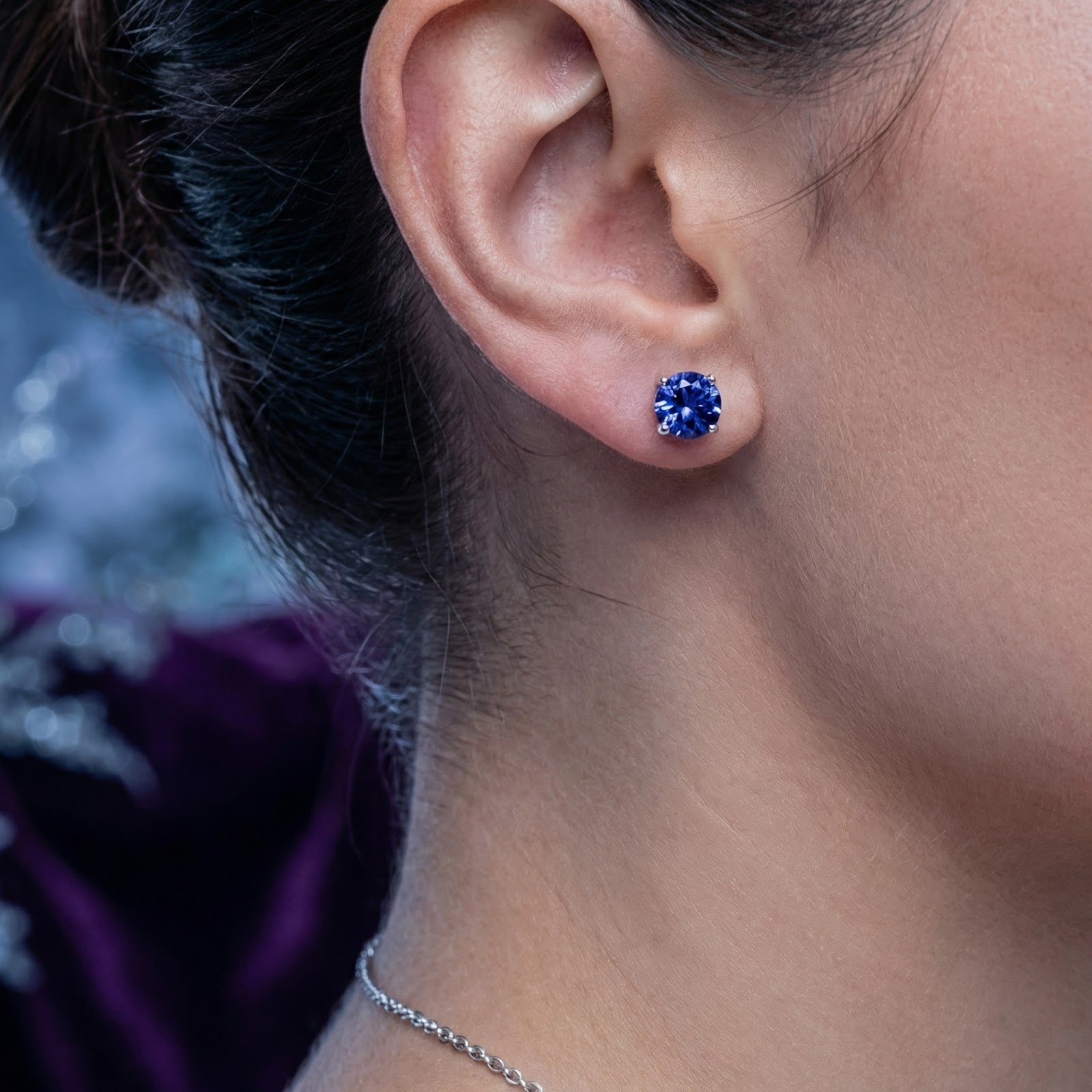 Close-up of a woman wearing a round cut simulated tanzanite and S925 sterling silver stud earring.