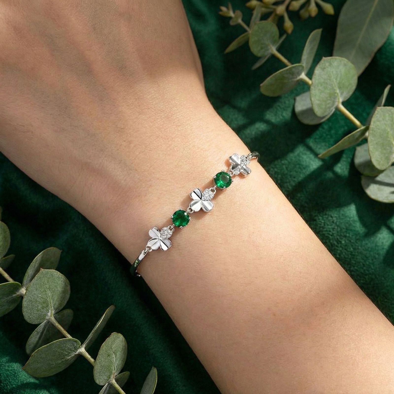 Close-up of the sterling silver clover charms and round green simulated emeralds on a person's wrist.