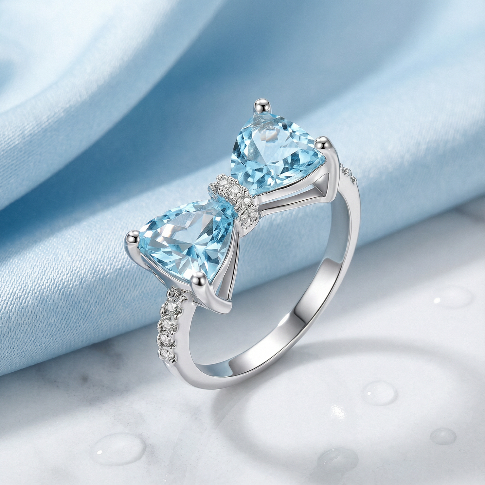 Trillion-cut simulated aquamarine bow ring in S925 sterling silver on blue silk with water droplets.
