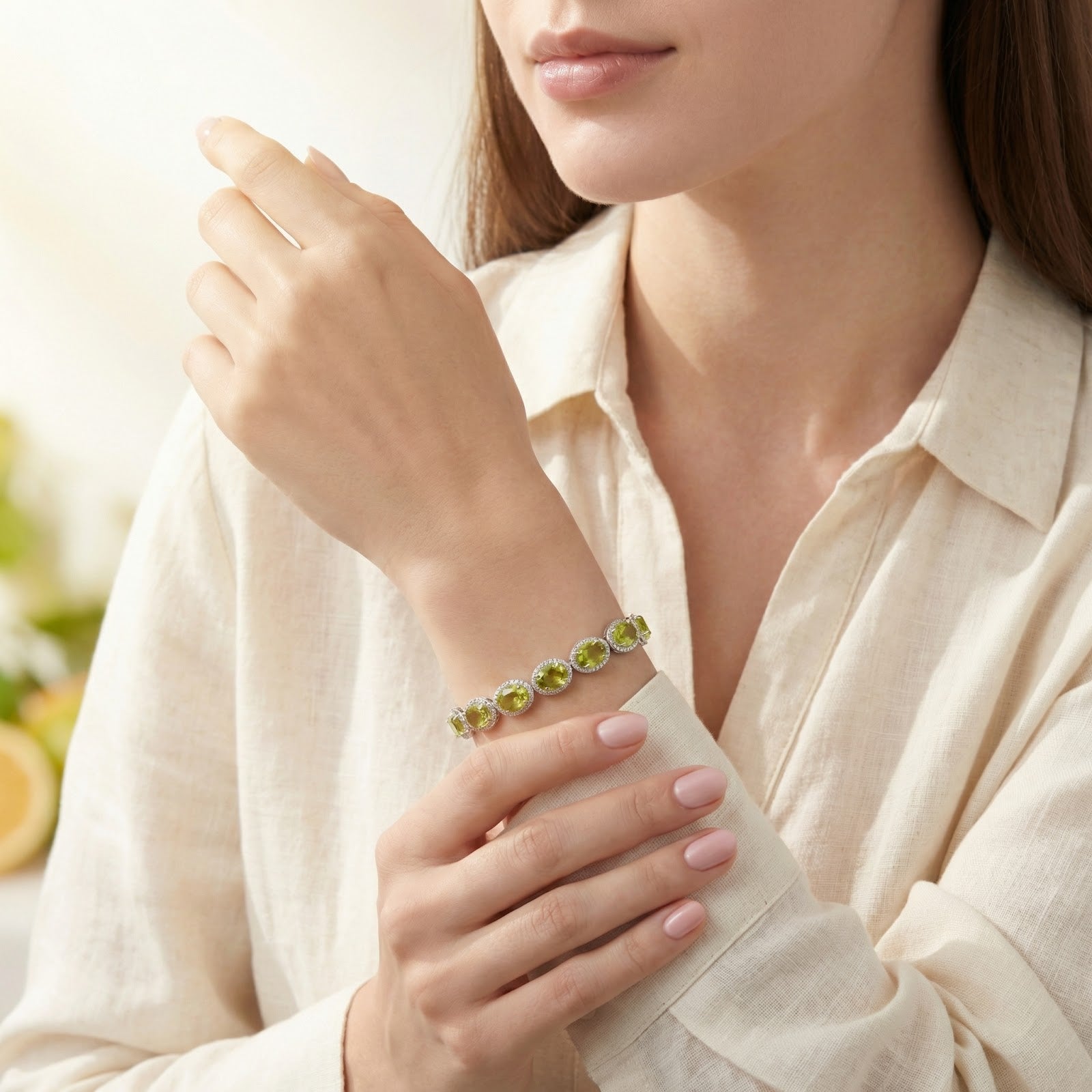 Woman wearing a sterling silver tennis bracelet with oval simulated peridot stones over a cream linen shirt.