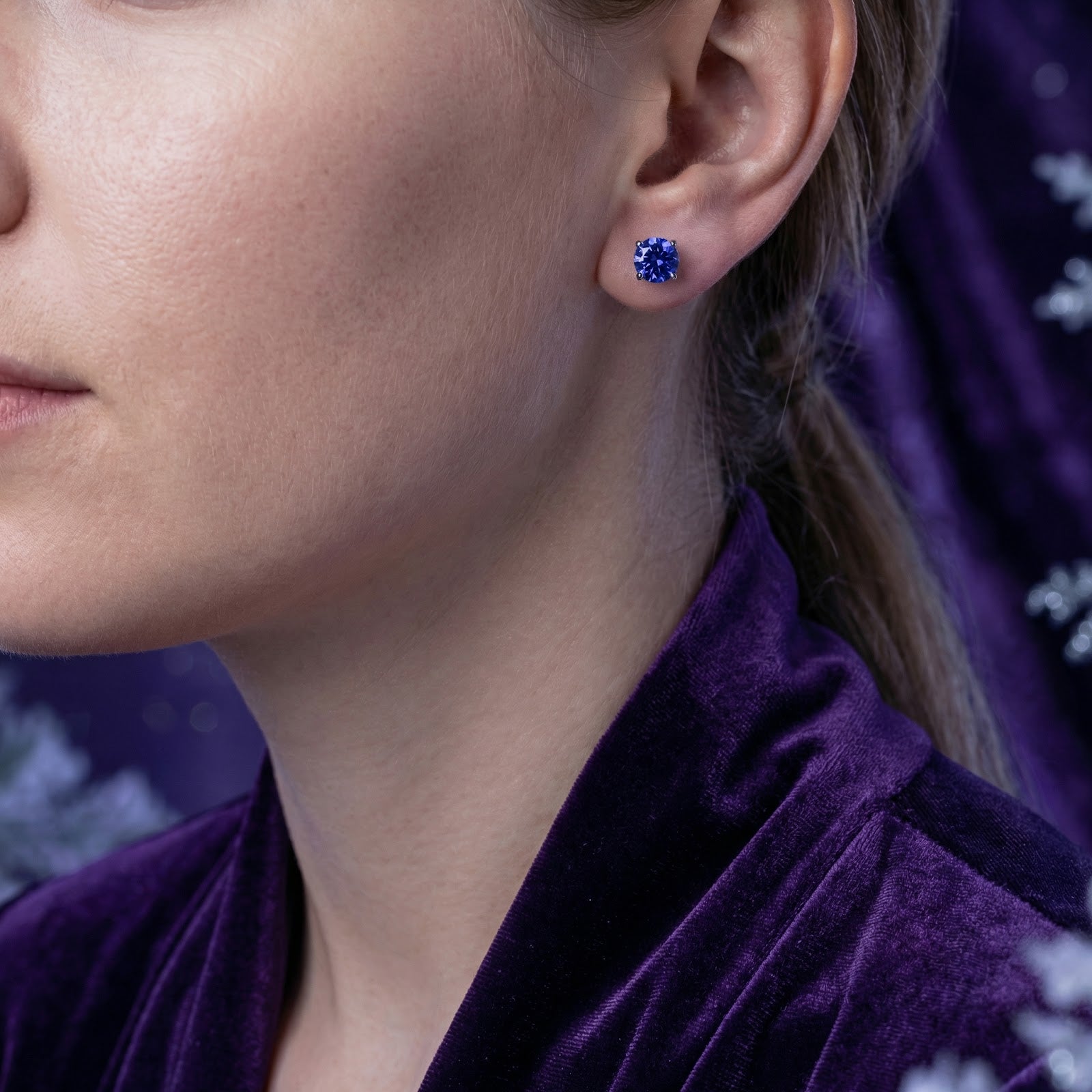 Woman wearing a round cut simulated tanzanite S925 sterling silver stud earring with a purple velvet top.